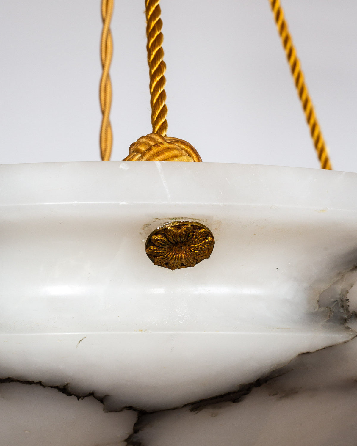 Close-up of the Spigel Art Deco Diamond Alabaster Pendant, showcasing a white alabaster bowl shade, gold-tone decorative hardware, and twisted gold hanging cords—ideal for adding statement lighting to any space.