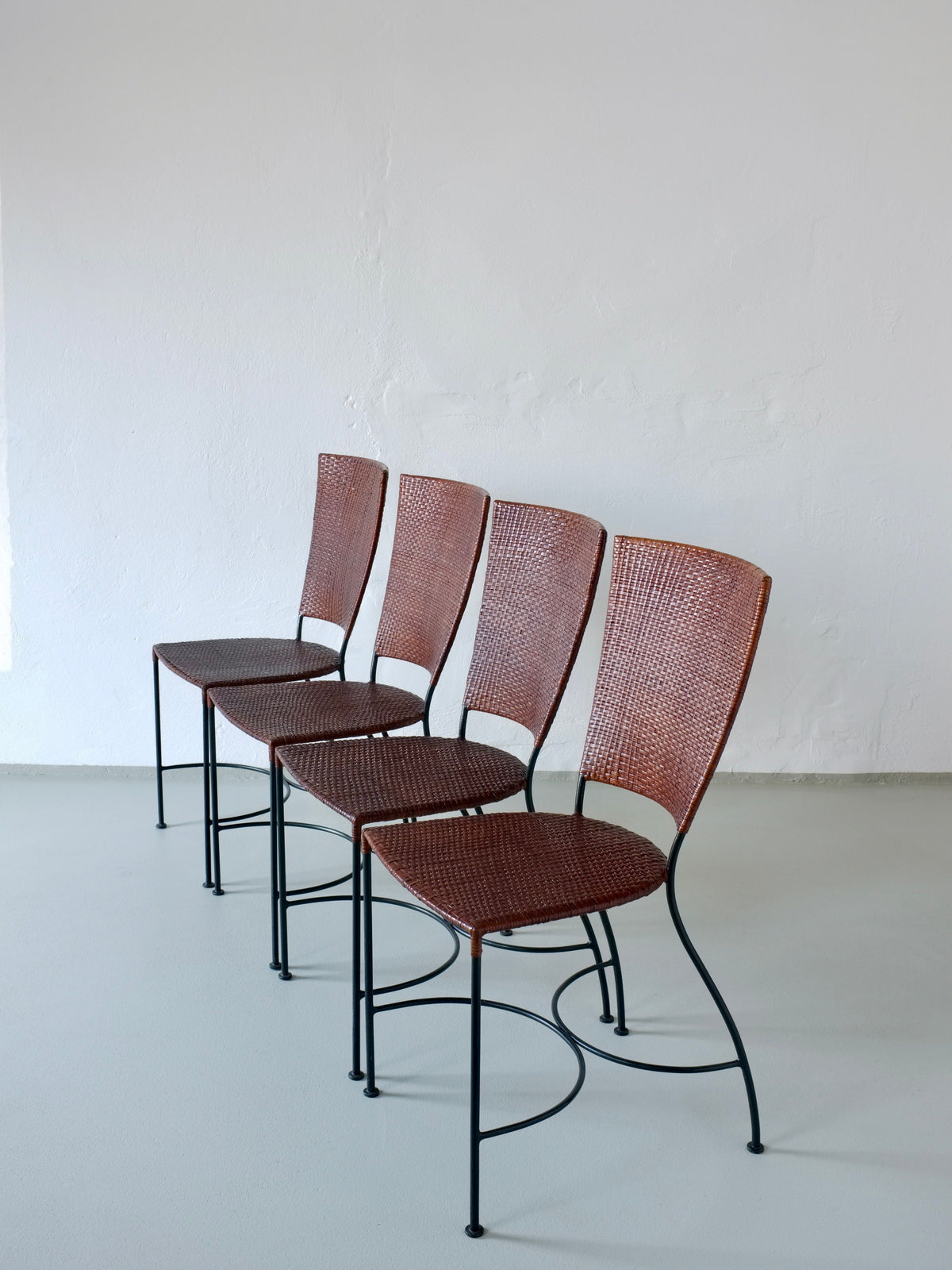 Four Belgian wrought iron chairs with woven rattan seats in row