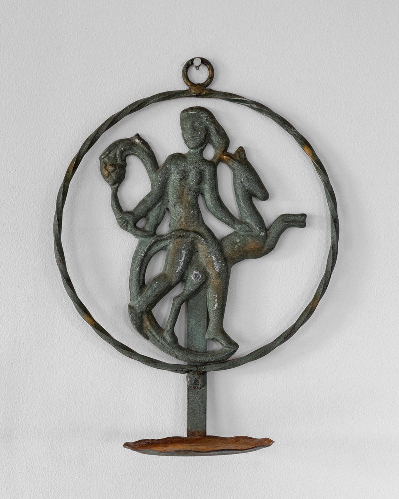 The Spigel Art Deco Wrought Iron Wall Sconce from 1920s/30s Sweden elegantly mounts on the wall, depicting a person riding a horse-like creature while holding another figure or animal. The metal's greenish patina adds an antiquated charm to this vintage piece.