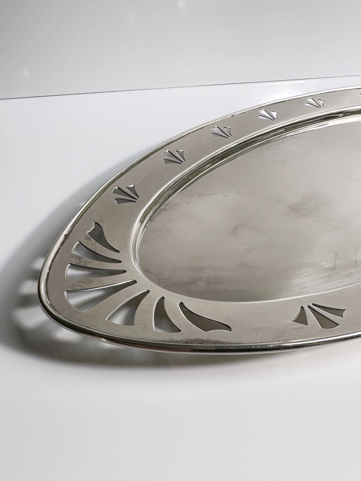 A silver oval serving tray from the Dodo Vintage 1930s Art Deco Silver Coffee Set features hotel silver plating and a decorative cut-out rim. The tray, partially shown on a white surface, echoes classic French Art Deco style.