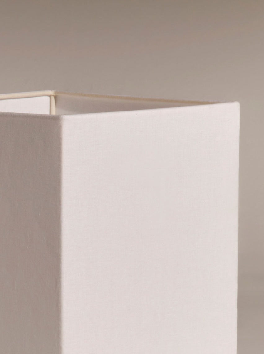 A close-up of a Nassi Lamps Roma I Squared White Travertine against a neutral background. The shade's fabric texture and sharp, clean edges are visible, showcasing simple, modernist design. The upper left corner of the lampshade is notably prominent in the image.