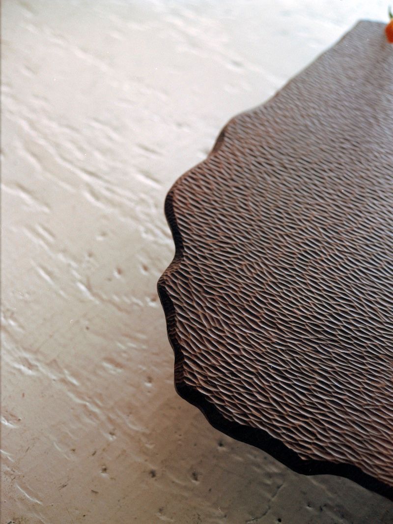 A close-up of the Mare Coffee Table by Ombia Studio, showcasing its textured, dark brown, irregular surface as it rests on a light textured background.