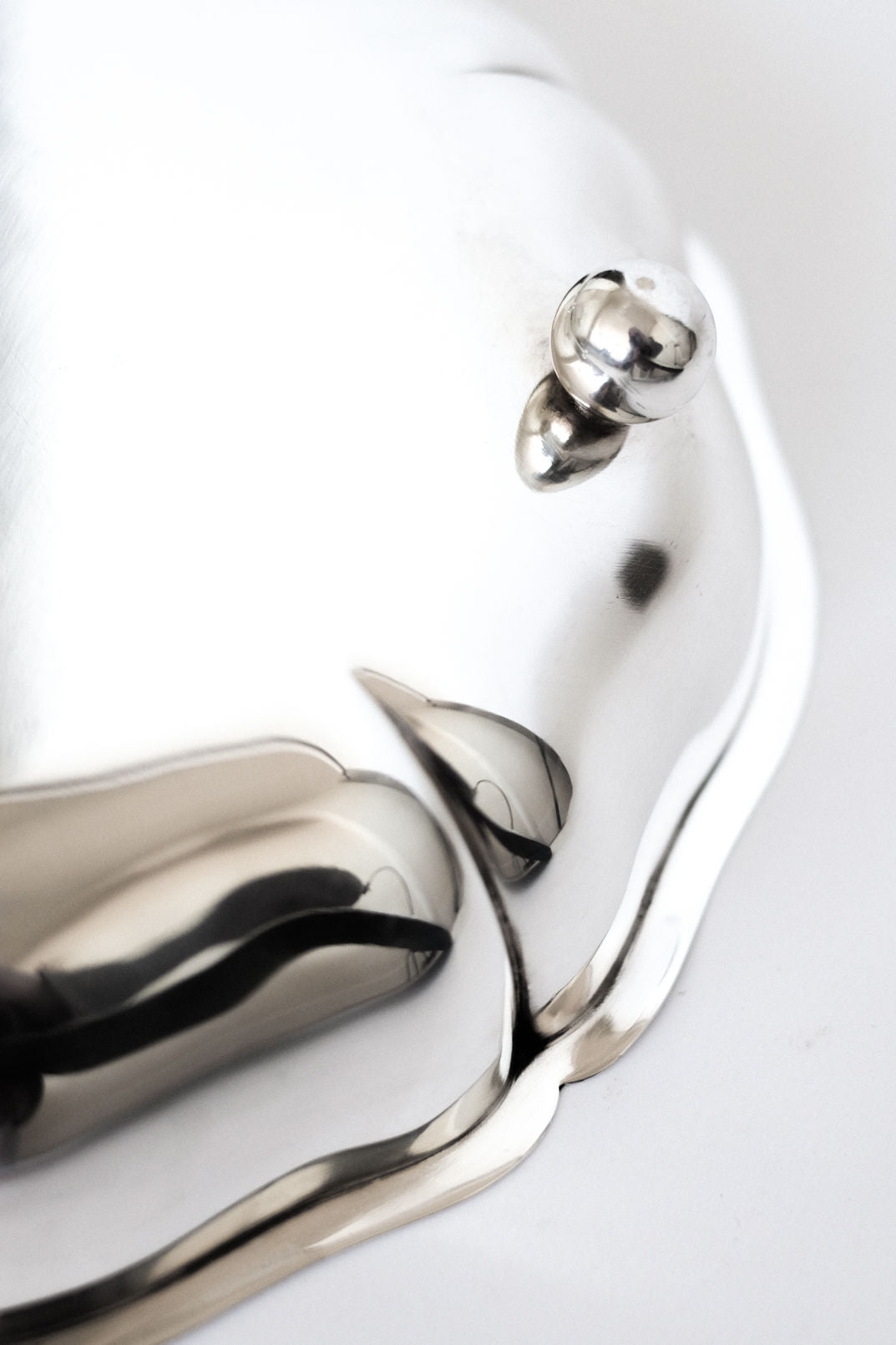 A close-up of the septembre studios Silver-plated Bowl shows its shiny, wavy-edged surface and round knob against a white background, highlighting the elegant silver finish.