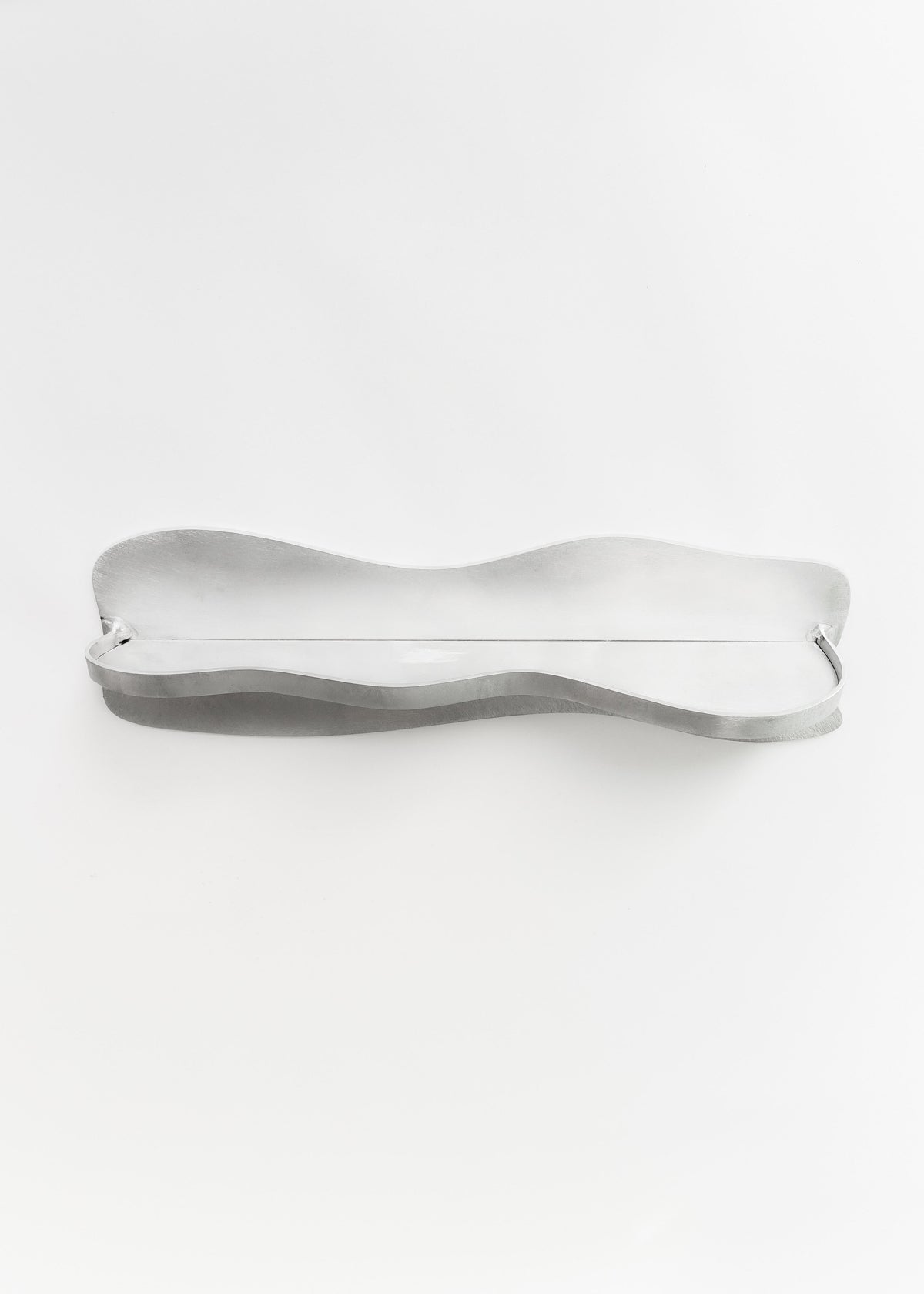 The Middle Shelf by Six Dots Design is a sleek, handcrafted tray with wavy edges and a polished finish. Its elongated design features a narrow middle and wider ends, forming an elegant curve with a smooth metallic surface ideal for any setting.