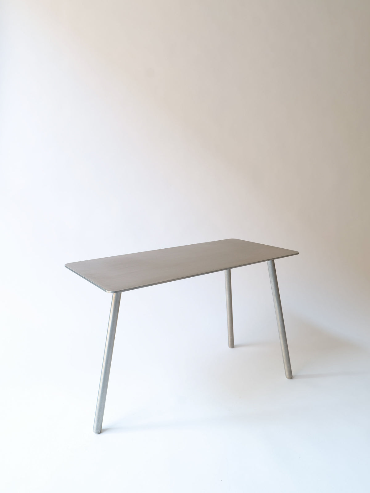 A minimalist, rectangular Collection apart Stick Table Jesper Morrison 2000 with a smooth, light gray surface and four simple, slightly angled legs. The background is plain and neutral, emphasizing the clean lines and modern design by Jasper Morrison.