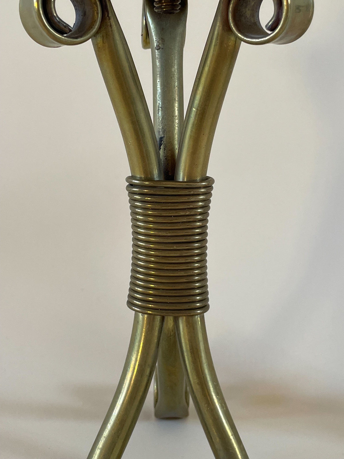 Close-up of a Pair of Mid-Century Danish Candleholders by Maud Vaughan with three curved legs bound together by coiled wire, reminiscent of Danish brass candleholders. The background is plain white, highlighting the shiny and slightly worn texture of the mid-century sculptural form.
