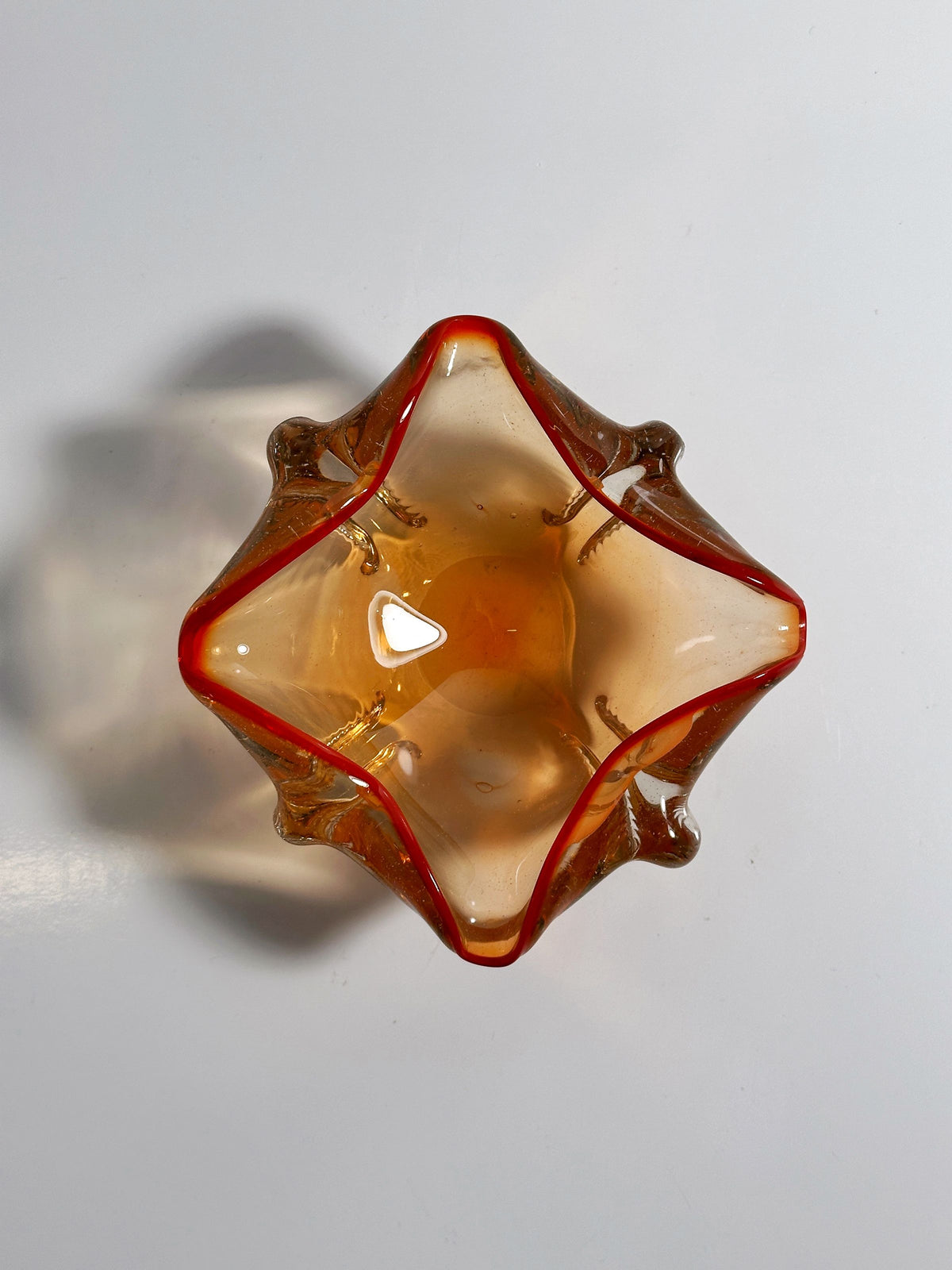 Top view of the Venetian Ashtray by Seguso Murano from the 1950s, a star-shaped, translucent coral-colored glass piece with wavy edges. The Dodo Vintage item has a nautical design that casts a soft shadow on the white surface beneath it.