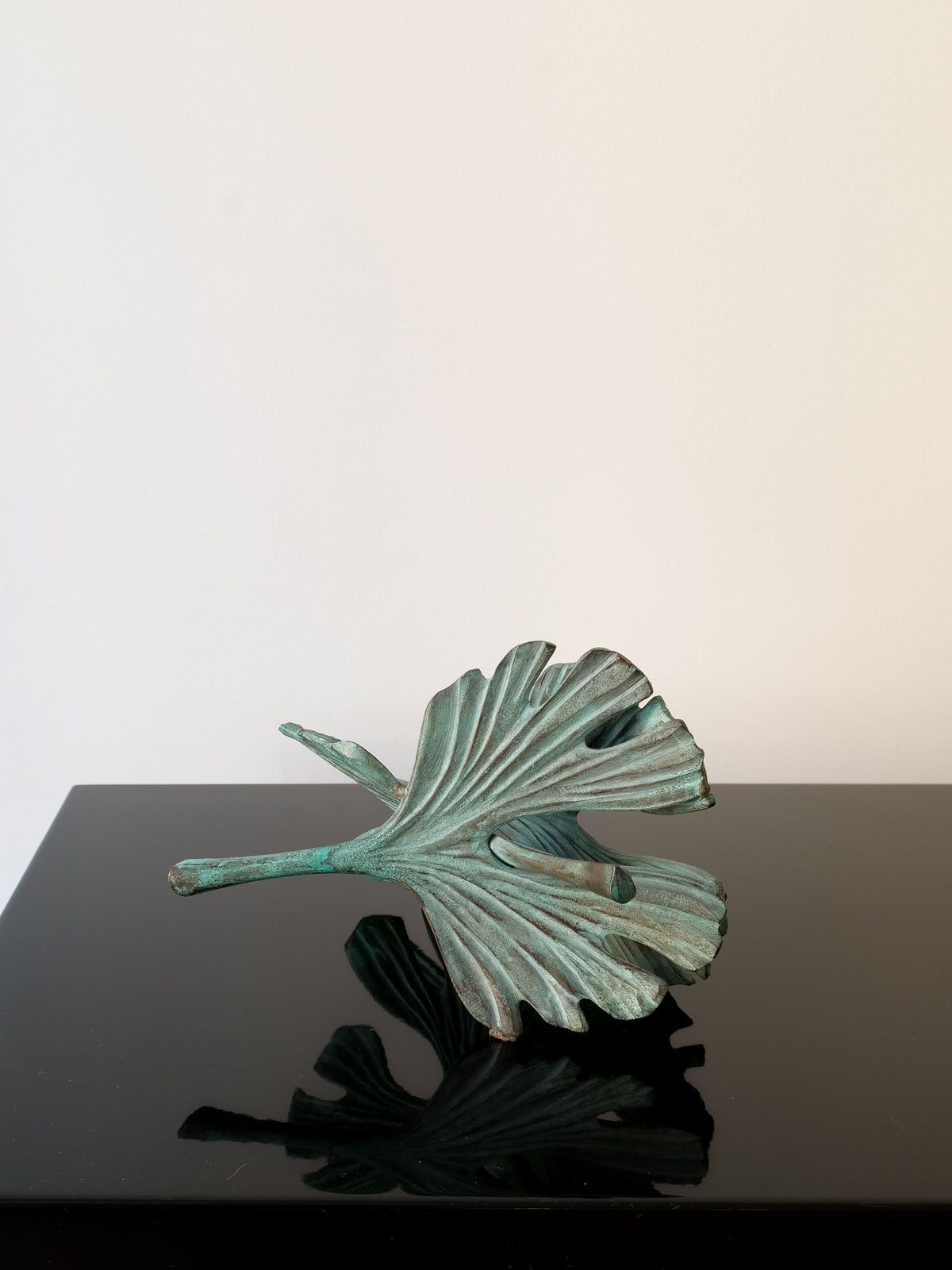 The Bronze Ginko Biloba Sculpture by Collection apart is a detailed, abstract piece featuring overlapping leaves on a glossy black base. Its teal patina offers a textured and organic look against a simple white backdrop.