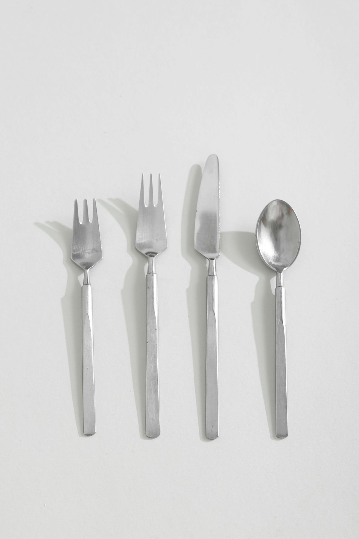 Four stainless steel Obelisk flatware pieces arranged in row