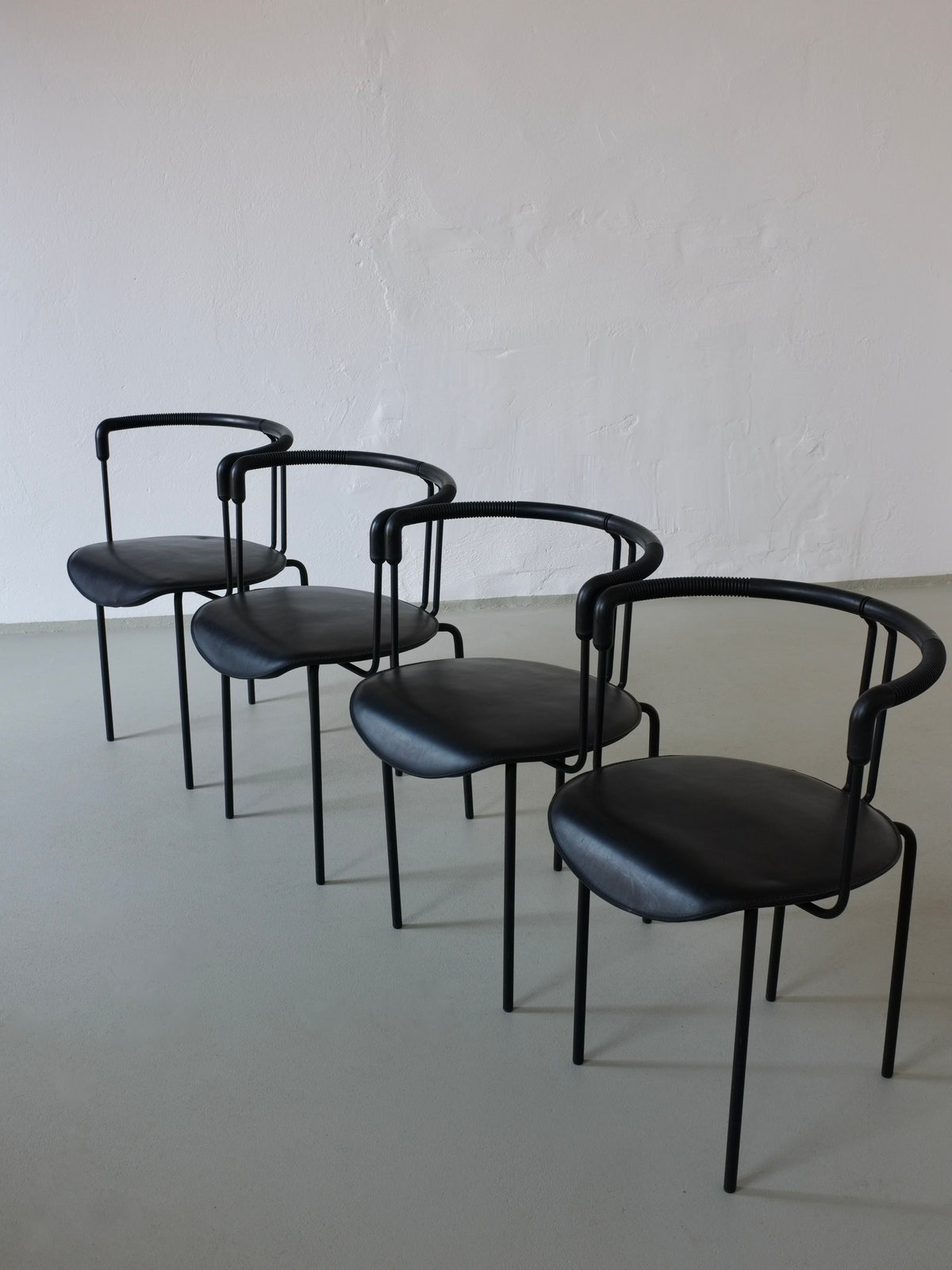 Four black leather postmodern armchairs arranged in perspective view