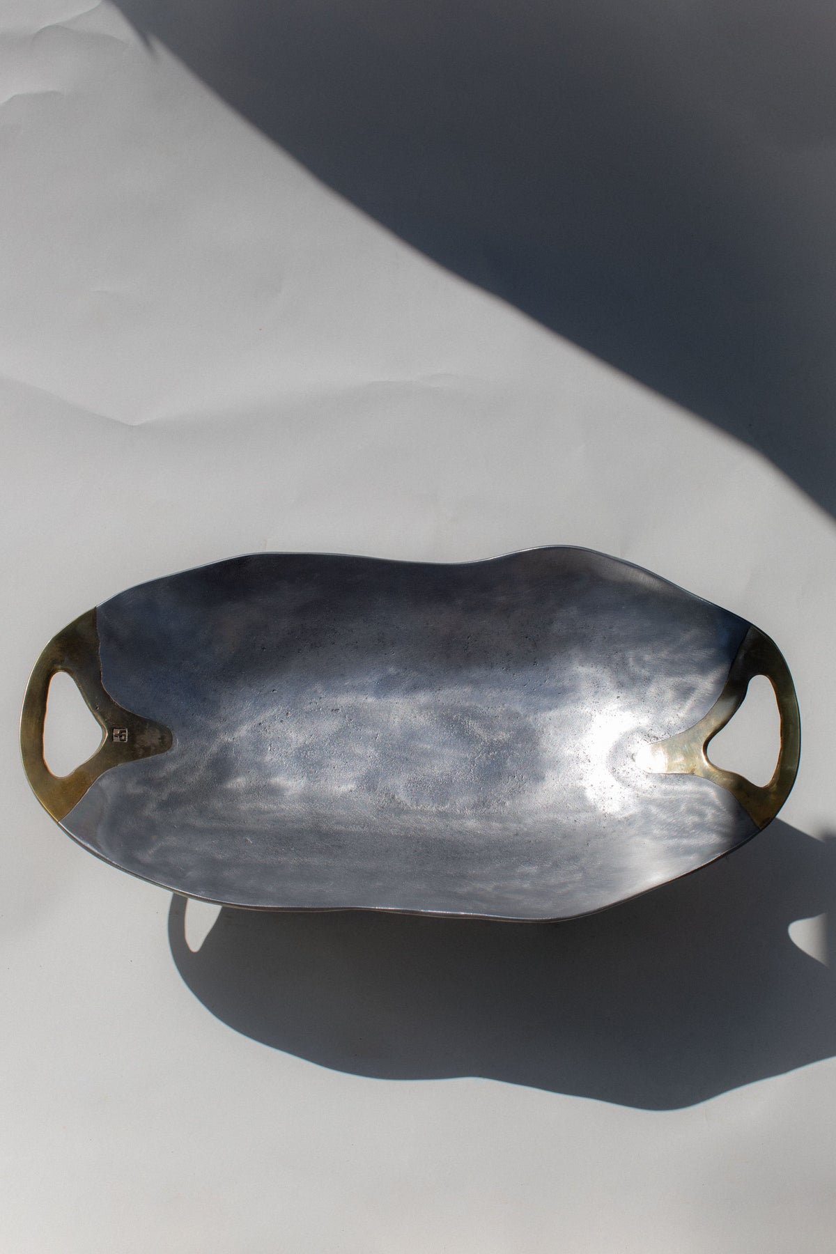 Dark metallic brutalist bowl with curved handles casting dramatic shadow