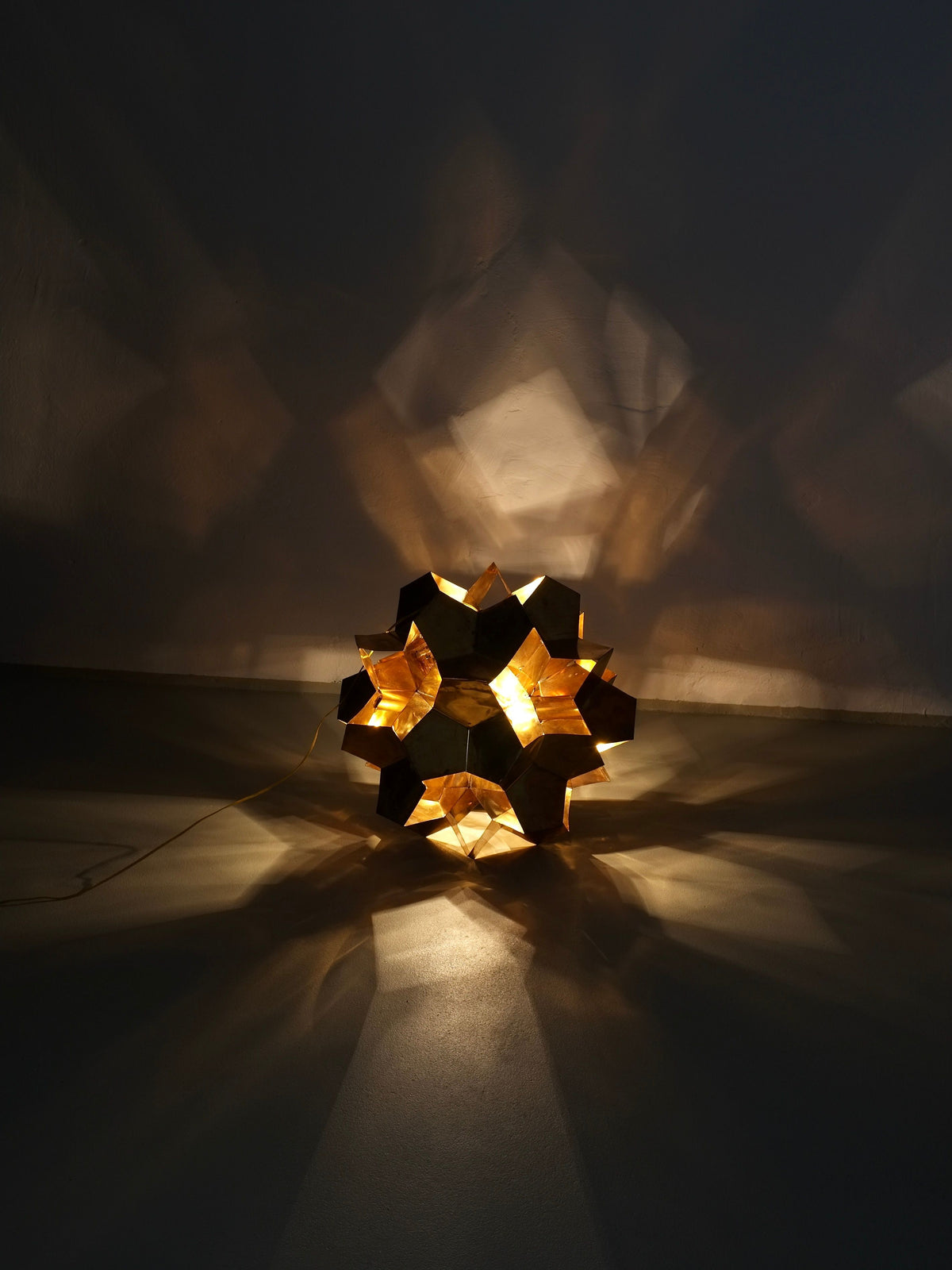 The Brutalist Brass Chandelier by Veter Vintage, Latvia 70s, emits warm light and creates sculptural lighting effects, casting star-shaped shadows and intricate patterns on surrounding walls and floors.