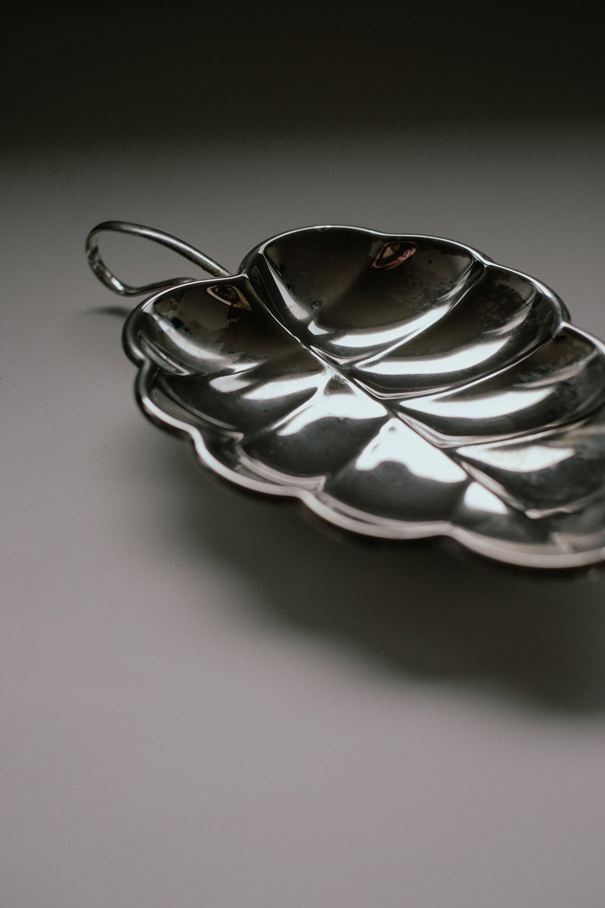 This Serving Dish Leaf by septembre studios exudes vintage charm with its silver, leaf-shaped design and handle. Resting elegantly on a light surface, its detailed veins mimic nature's beauty, while a subtle shine enhances its exquisite metallic texture.