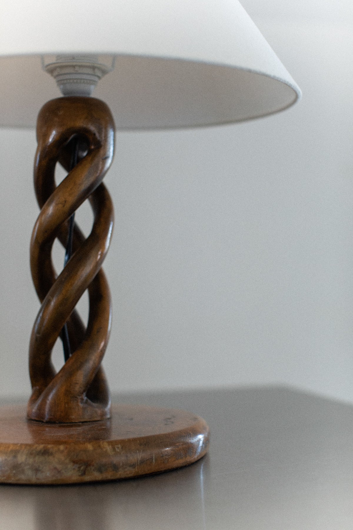 An Early-Century Lamp by Out For Lunch, featuring a handcrafted white shade and a twisted wooden base, rests on a smooth brown surface. Its distinctive double helix design enhances the simple, modern ambiance with an artistic flair.