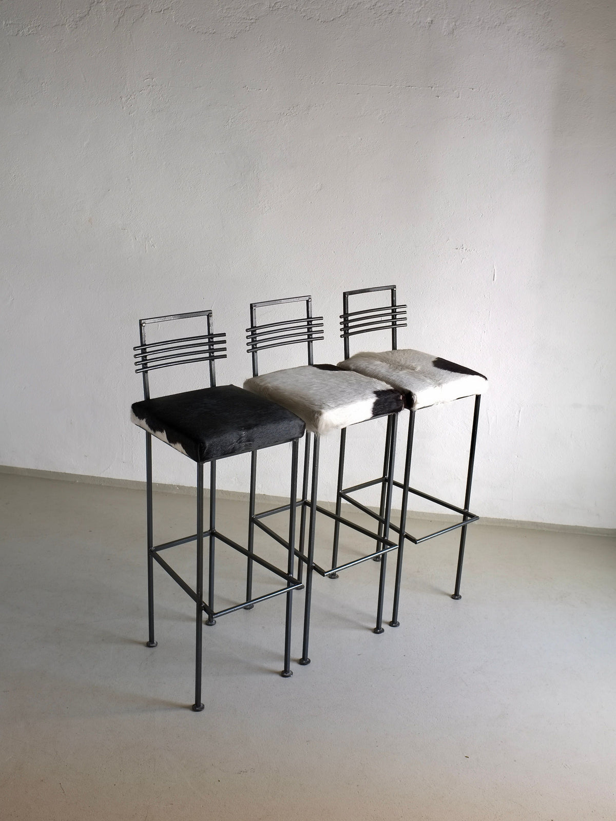 Three wrought iron bar stools with cowhide seats, minimalist design