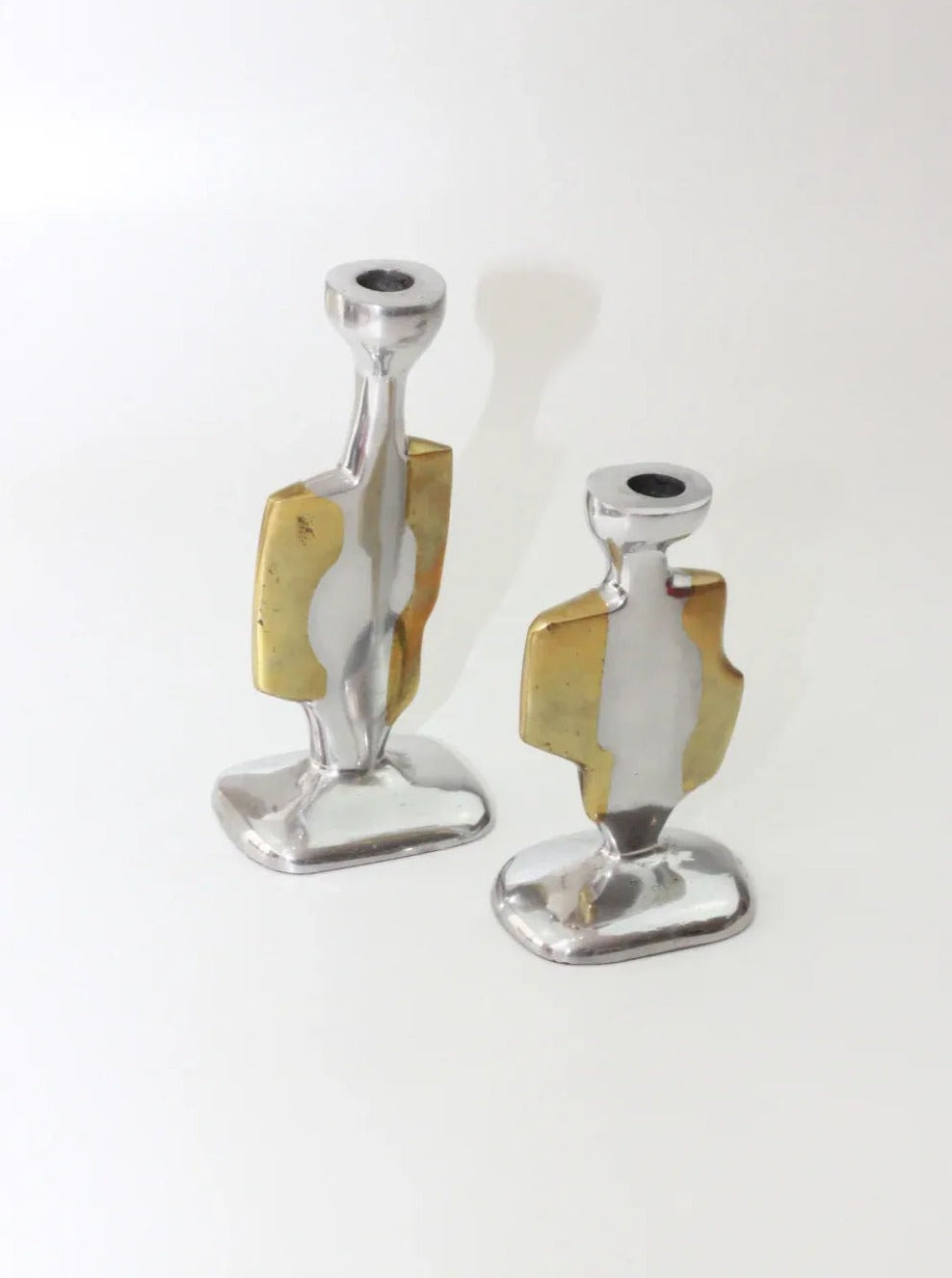 A pair of Brutalist Candleholders by Boga Avante Shop, crafted with a unique abstract design and polished silver and brass accents, reminiscent of David Marshall's vintage style, stand upright on a plain white surface against a plain white background.
