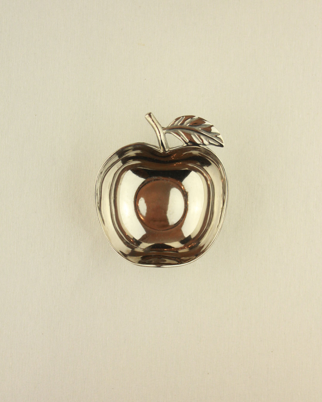 The Boga Avante Shop Decorative Apple Shaped Dish features a small, shiny silver finish with a leaf accent, ideal as a stylish accent or small serving bowl on any light-colored background.