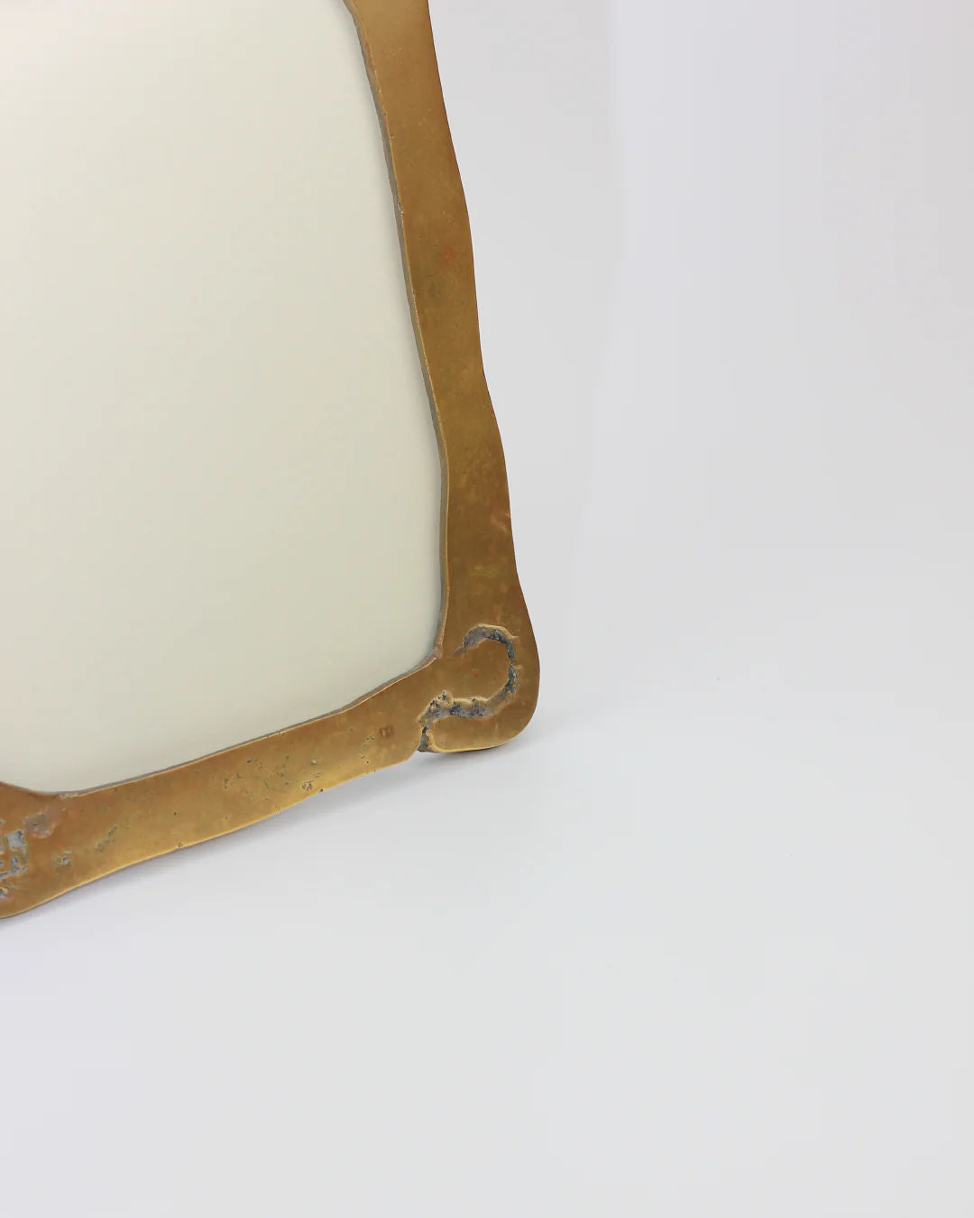 Close-up of the Brutalist Mirror by Boga Avante Shop, showcasing an ornate gold-finished corner with a decorative scroll design against a plain light background, subtly contrasting its minimalist style.