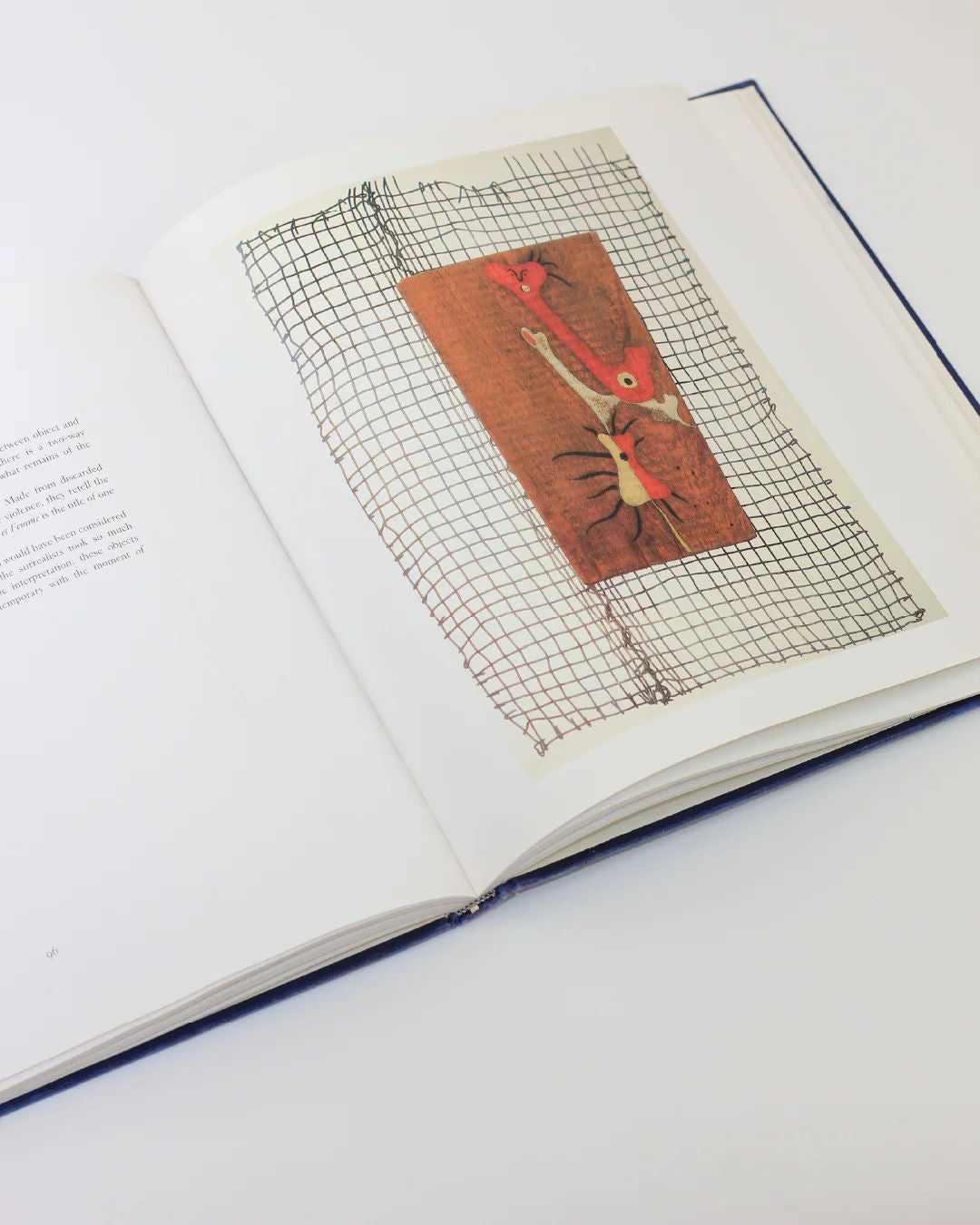 The Mirò The Masterworks Book by Boga Avante Shop is open to a page with abstract, modern art—a grid pattern on brown canvas with red and white. The opposite page has text, reminiscent of Joan Miró's surrealism, set against a pristine white backdrop.