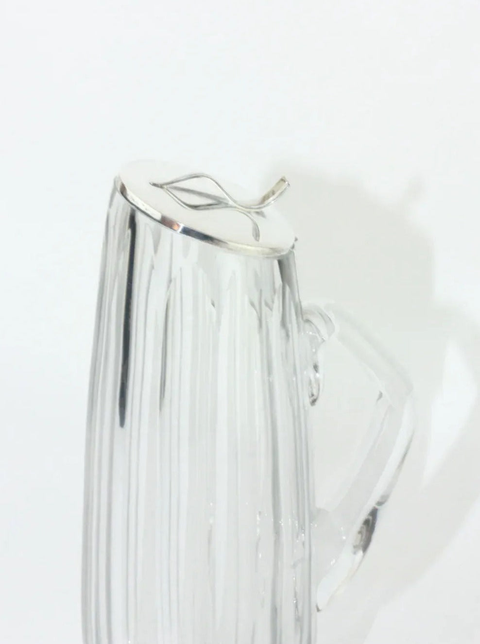 A Boga Avante Shop Crystal Decanter features a clear, ribbed glass pitcher with a handle and a shiny silver-plated lid adorned with a leaf-shaped knob on top. This handmade 60's/70's piece is photographed against a plain white background, casting an elegant shadow on the surface.