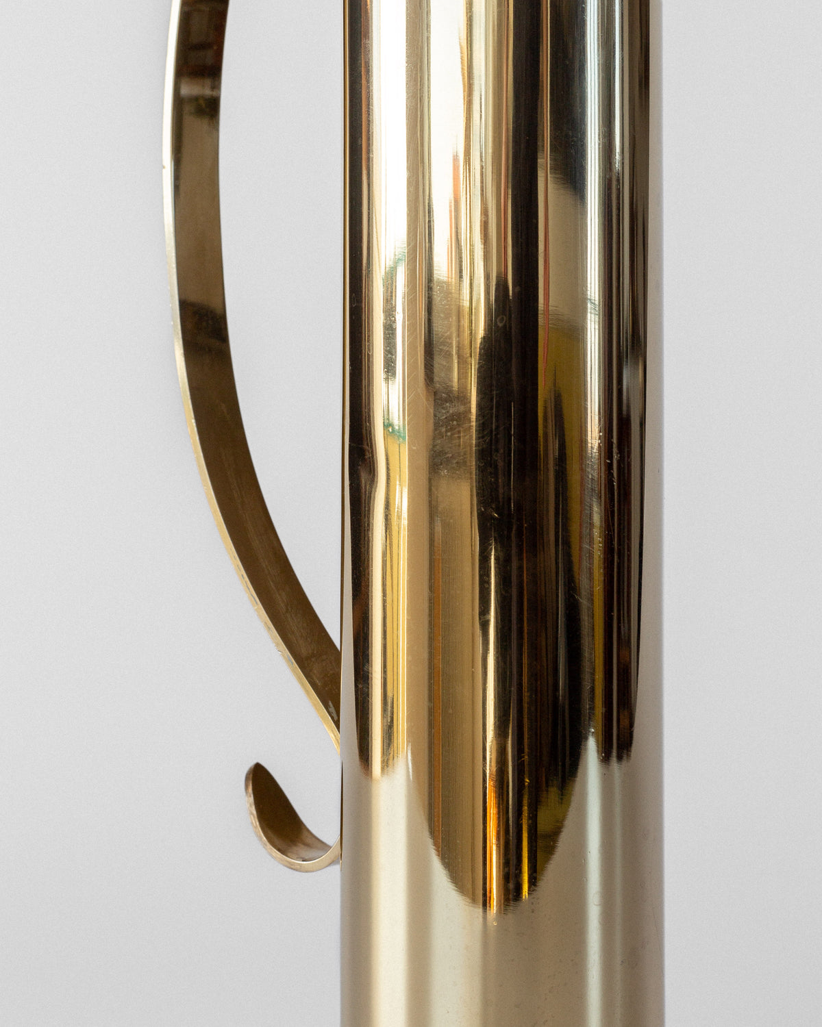 Close-up of the Spigel Large Mid-Century Brass Vase’s shiny, reflective handle on its cylindrical metallic surface, set against a plain light gray background.