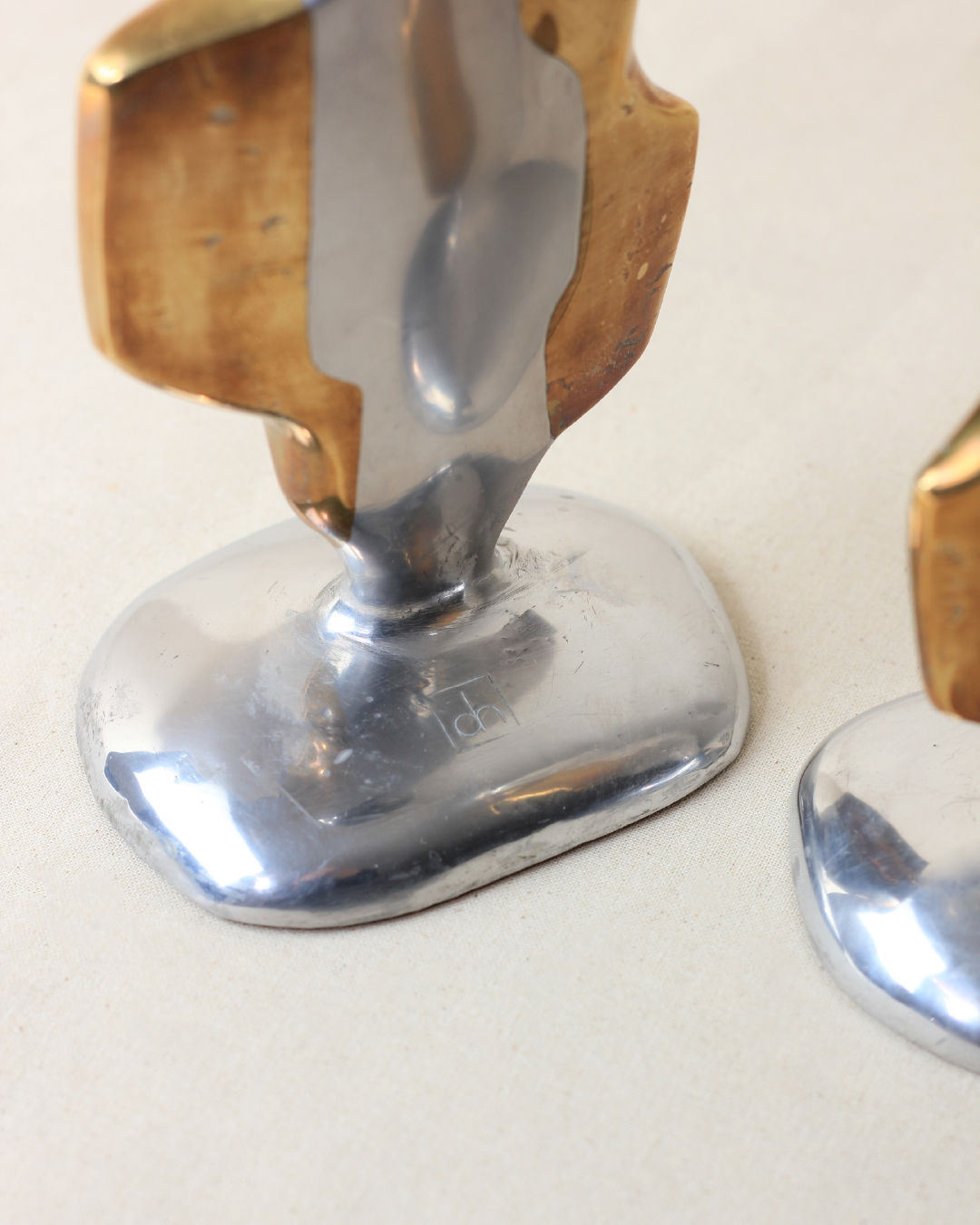 Close-up of the Pair of Brutalist Candleholders by Boga Avante Shop, featuring a shiny silver base and abstract upright gold and silver forms, shown standing on a light-colored surface.