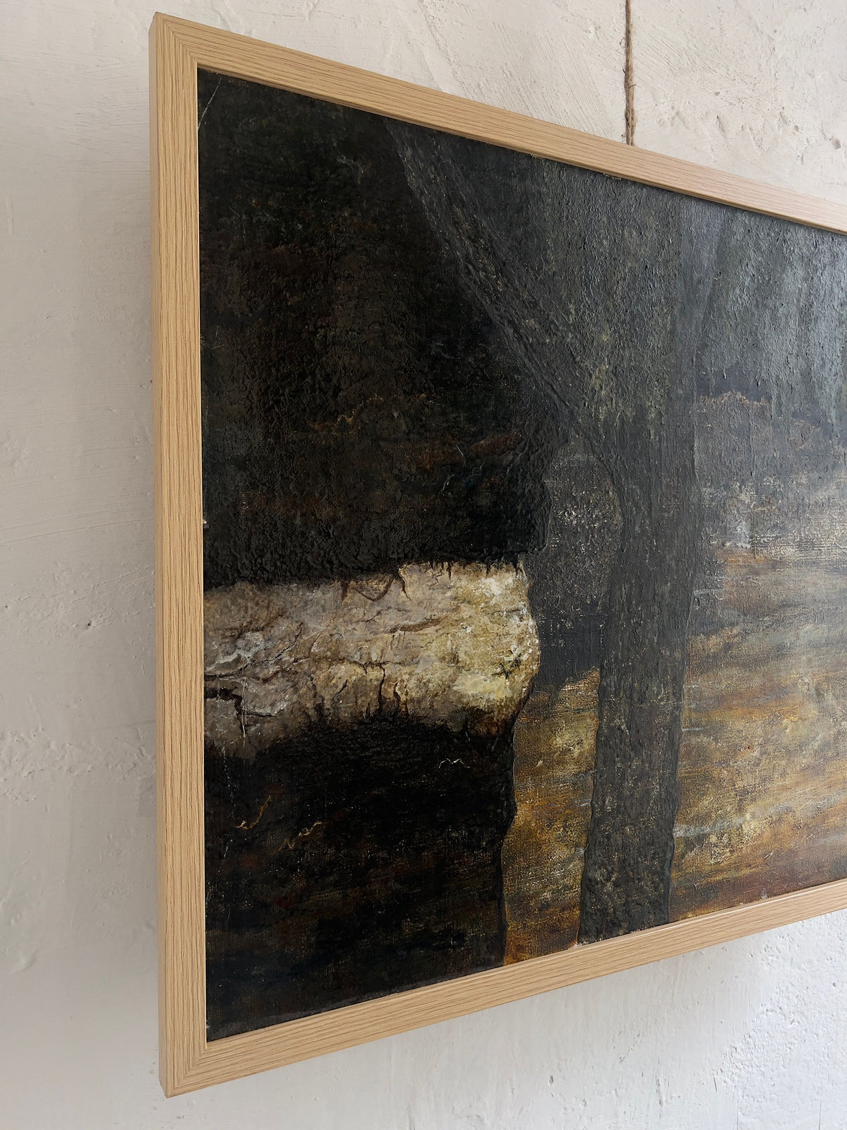 A side view of Veter Vintage's Vintage Landscape Painting, Oil on Canvas, framed against a white wall. It features abstract earthy tones with textured layers in dark browns and blacks highlighting natural elements, complemented by a lighter streak. The wooden frame has a light, natural finish like classic Netherlands artistry.