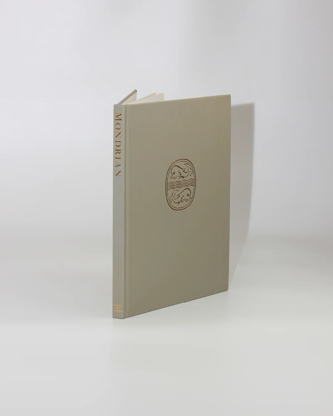 A beige hardcover book titled "Mondrian" by Hans L.C. Jaffé from Boga Avante Shop features a minimalistic circular emblem gracing the cover. It's an homage to Piet Mondrian's abstract art and neoplasticism, standing slightly open against a light gray background.