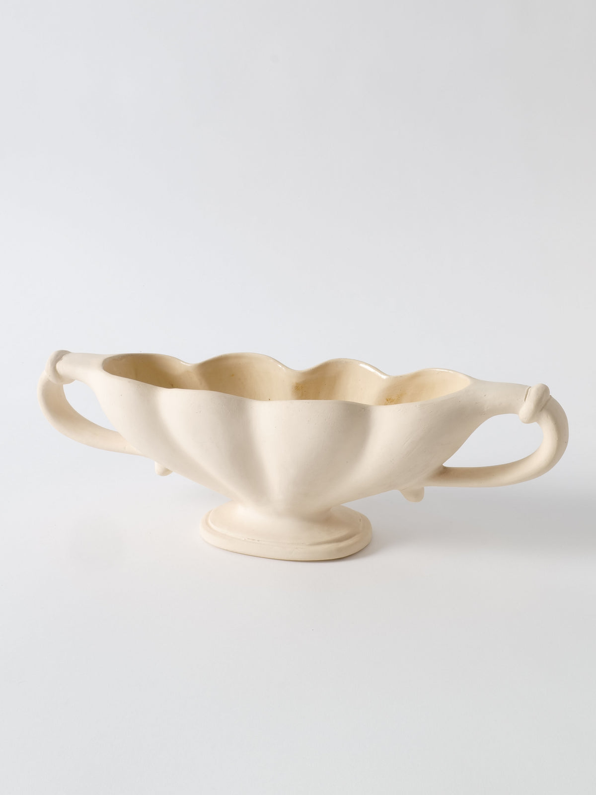 A cream-colored, ceramic serving dish with two symmetrical, ornate handles. The dish has a scalloped edge and a slightly elevated base, giving it an elegant, vintage appearance. Made from Devon clay by Collection apart, the background is plain white.