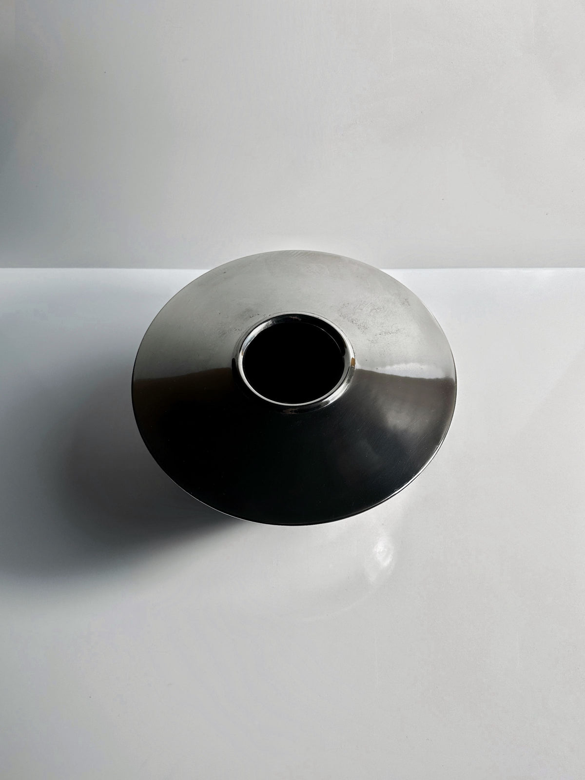 The Heavy Silver-Plated Vase by Dodo Vintage from Fink Germany is a metallic, reflective, donut-shaped object with shadows and highlights accentuating its glossy texture, reminiscent of 1980s jewelry design.