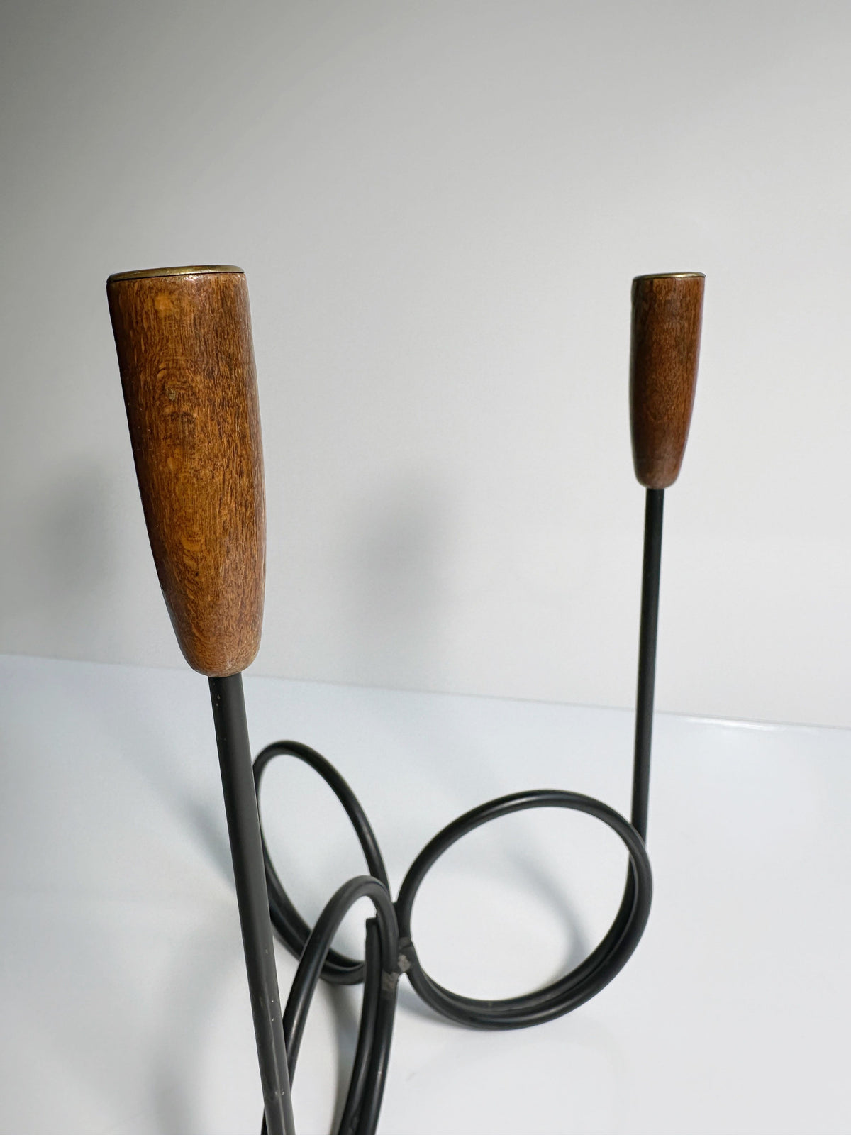 A close-up of a sleek, modern Danish Candleholder from the 1960s, by Dodo Vintage. The candleholder features minimalist black metal loops designed to hold candles with polished teak ends at the top of the handles, set against a neutral background.