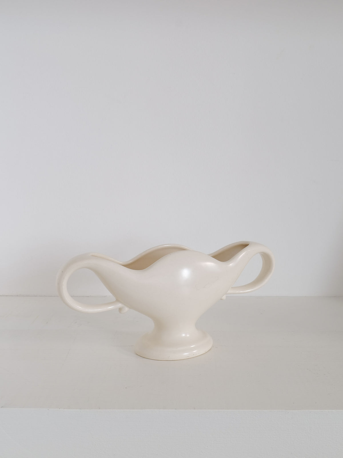 A white, double-handled ceramic vase with a wide, waved opening sits centered on a plain, white surface against a light gray background. This vintage Mini Mantle Vase 1930s by Collection apart features a glossy finish and a sturdy base.