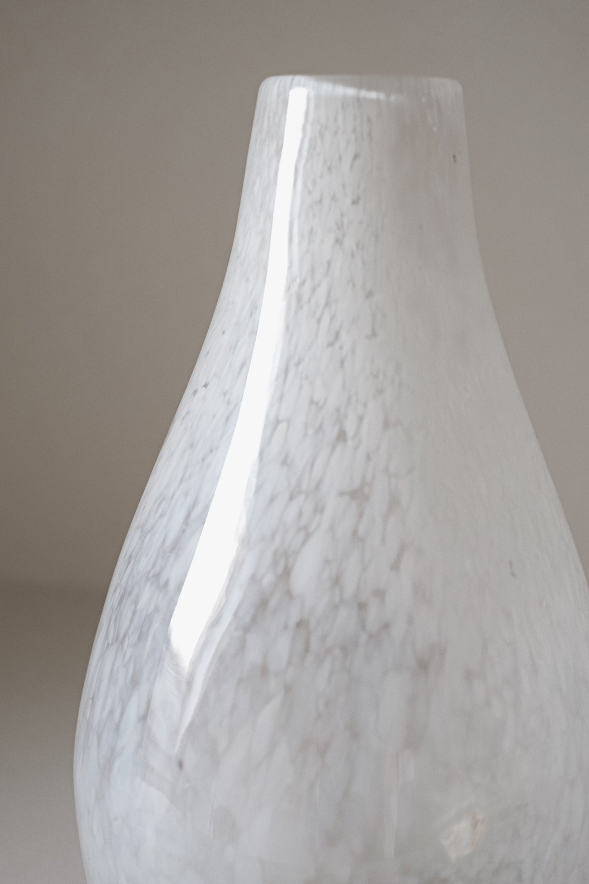 A close-up of the White Vase Tortoise Glass by septembre studios reveals its glossy white finish with subtle gray marbling and smooth, curved shape, highlighting its unique character against a plain light background.
