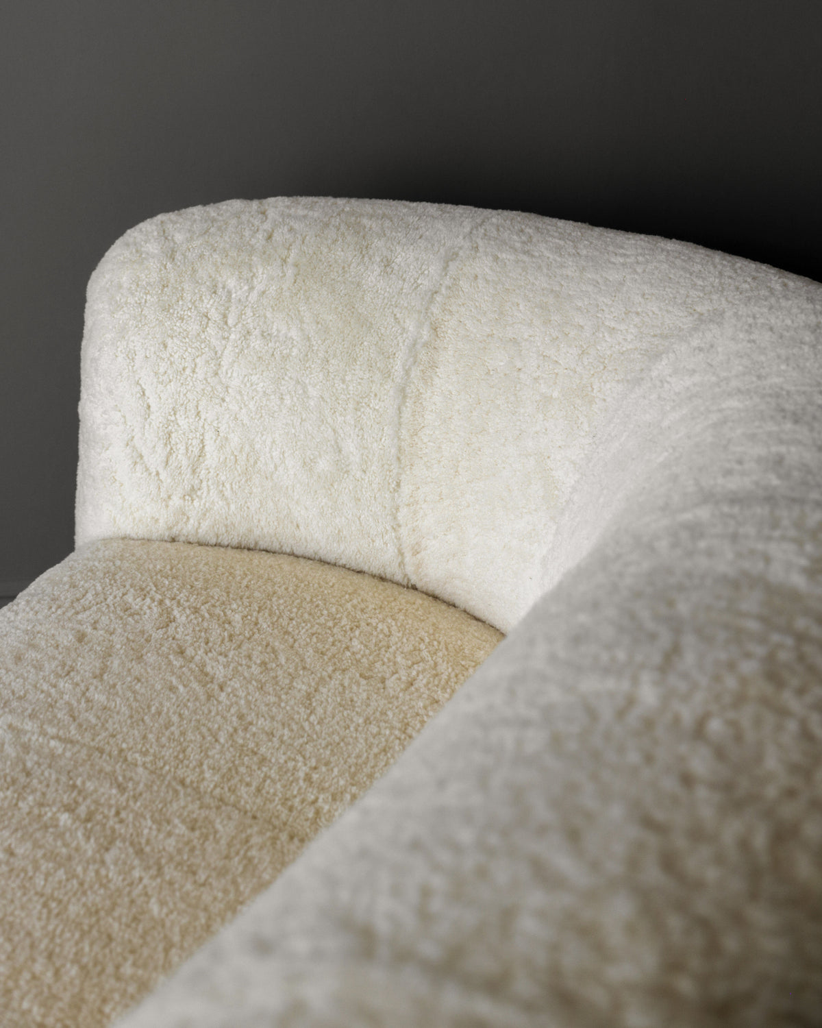 Close-up of the Fritz Hansen Sofa in Shearling by Studio OSKLO, featuring soft off-white shearling upholstery and a sleek curved design, set against a plain gray background.