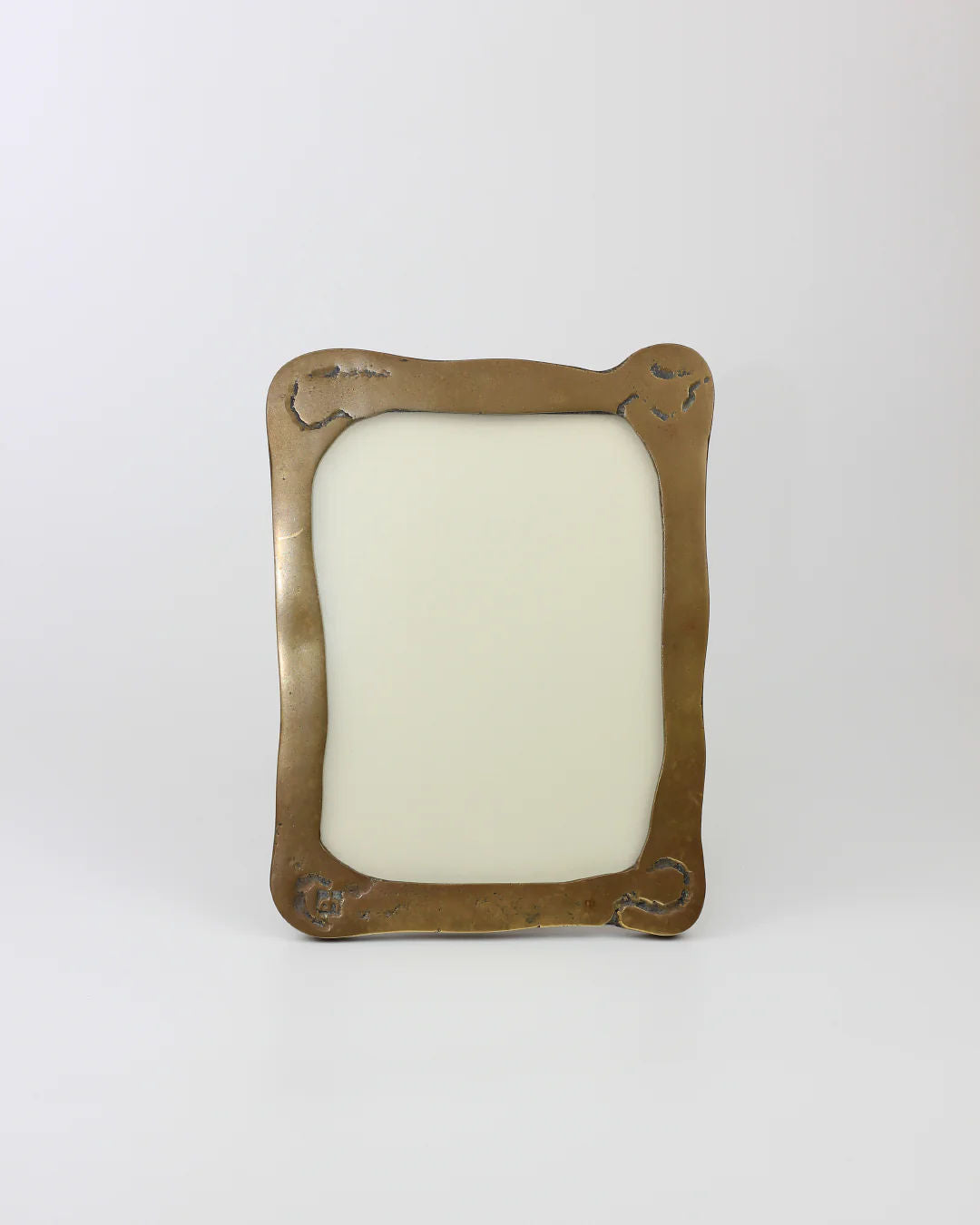 The Brutalist Mirror by Boga Avante Shop is showcased against a neutral background, highlighting its minimalist design. Its plain brass frame has a rounded rectangular shape with slight corner etchings, offering understated elegance that suggests an industrial finish.