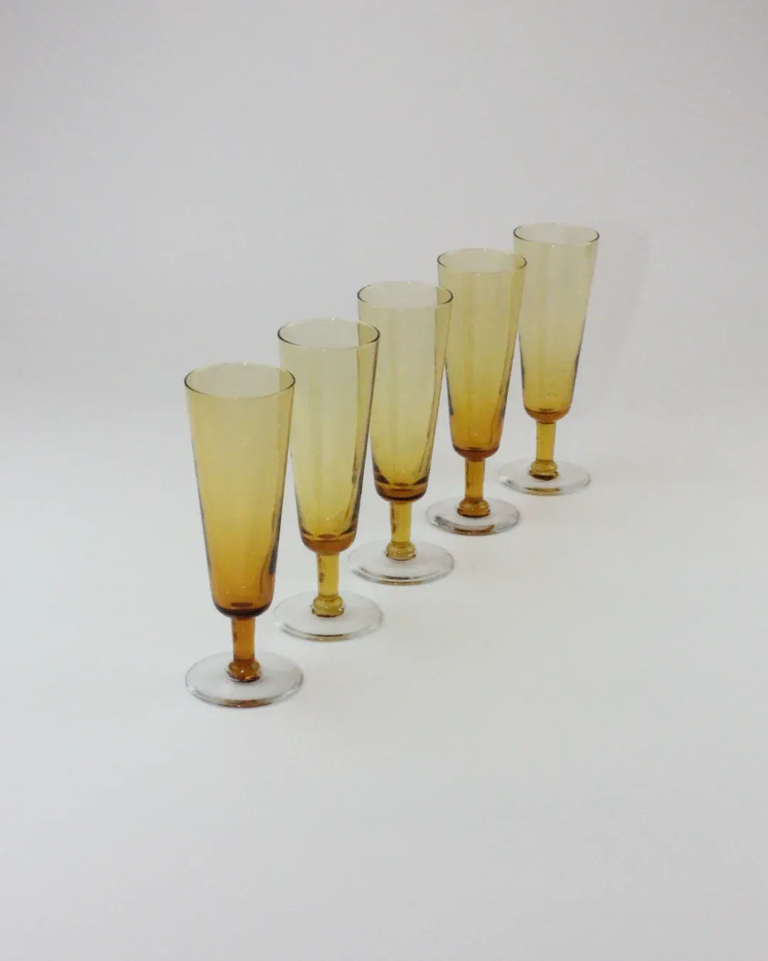 Five amber crystal champagne flutes arranged in diagonal line