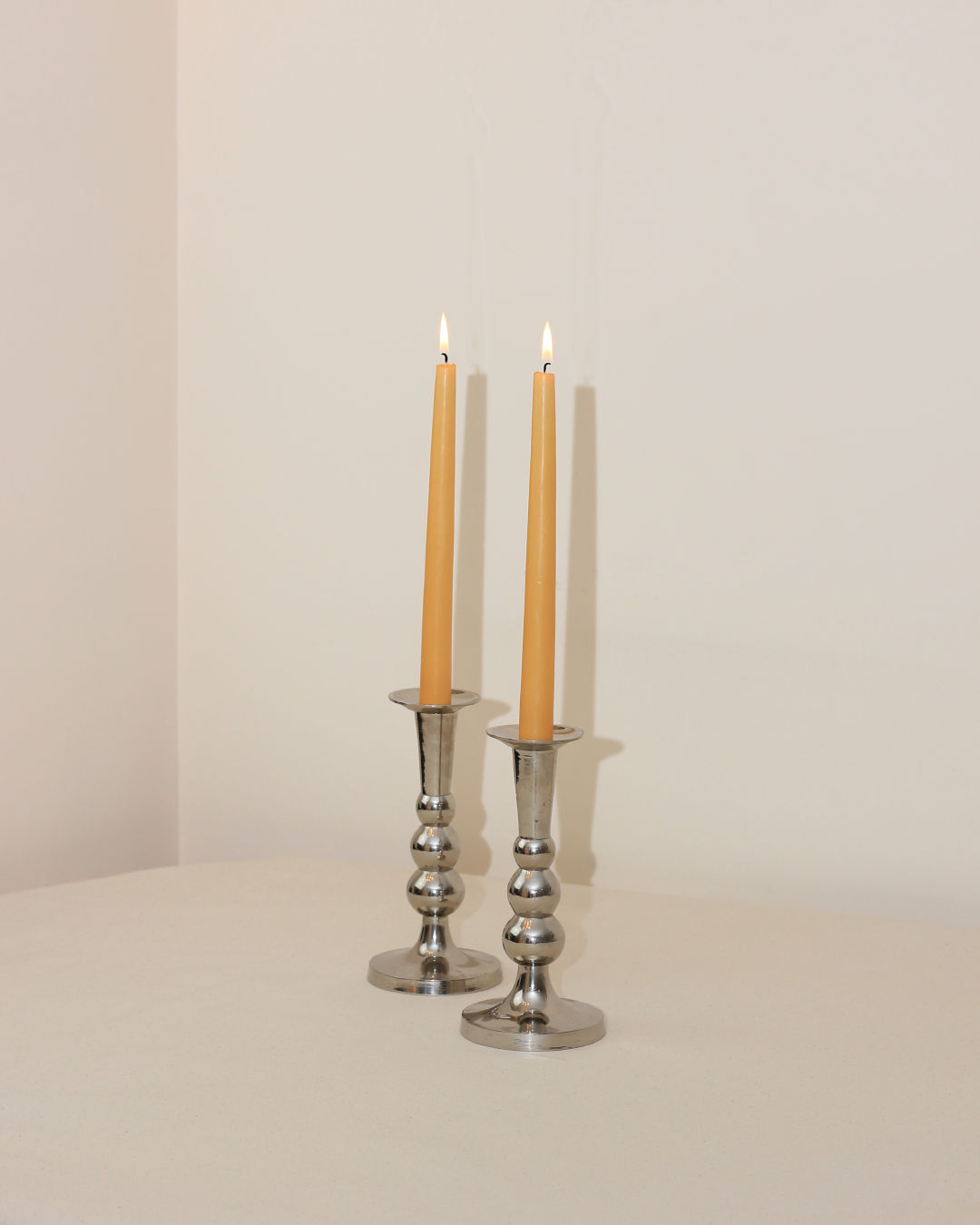 Two polished chrome Acero candleholders with lit taper candles