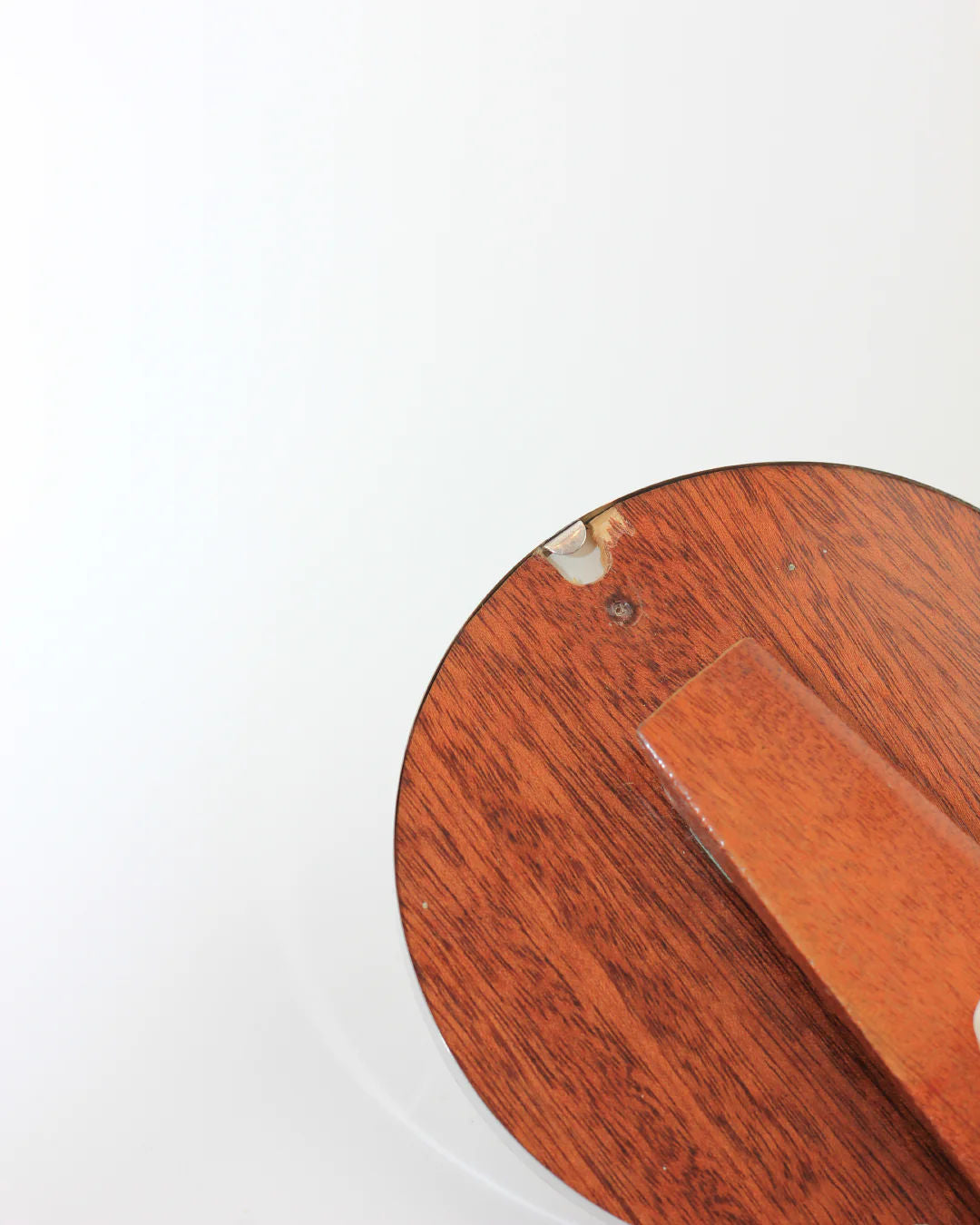 Close-up of a Boga Avante Shop round wooden table with a small chip on the edge, featuring a brown rectangular Round Art Deco Mirror resting on it against a plain white background.