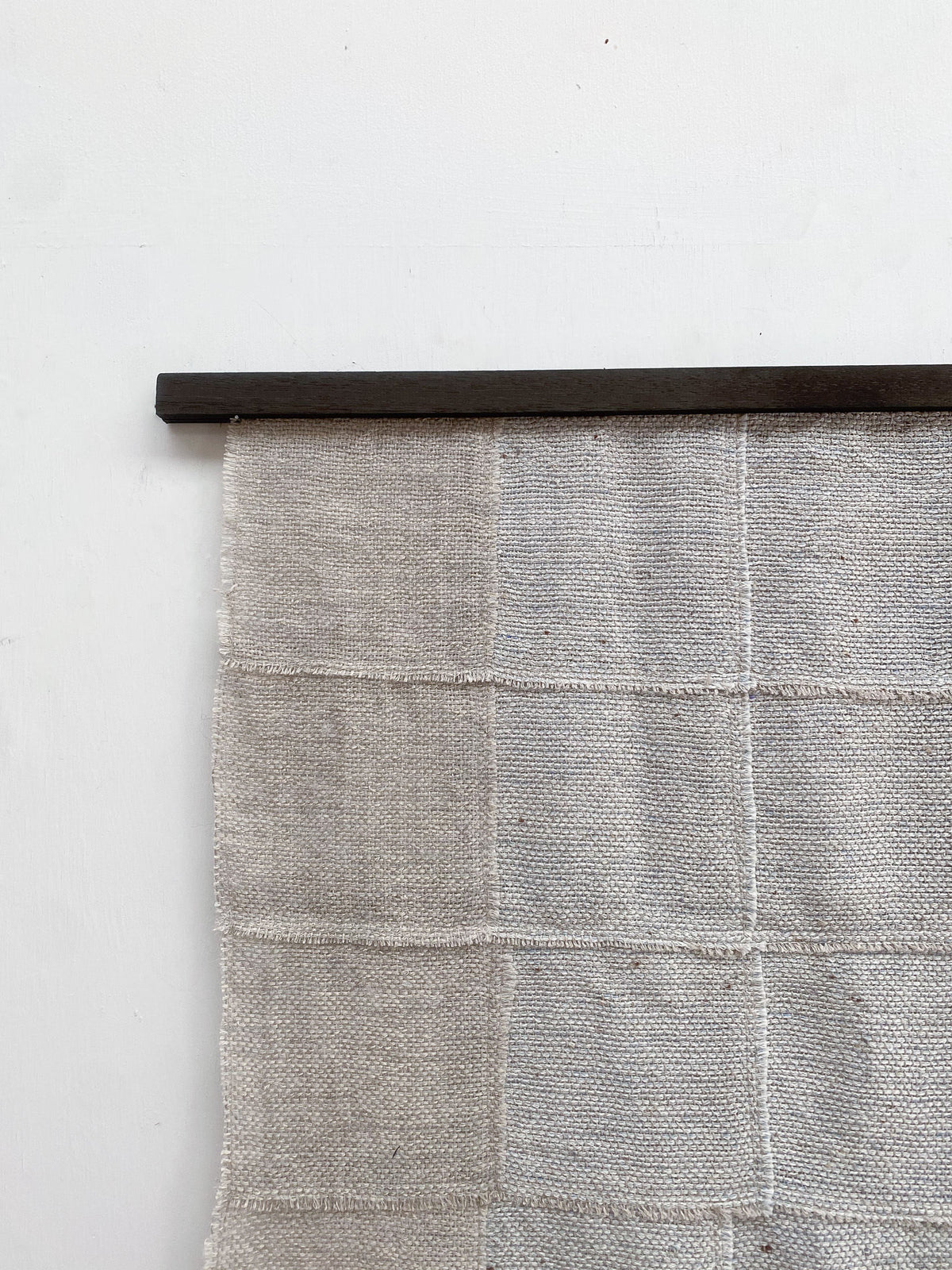 The "Blue Sky" Artwork by Sundance Studio, a woven wool-cotton wall hanging with a grid pattern, is displayed on a slim dark wooden rod against a plain white wall.