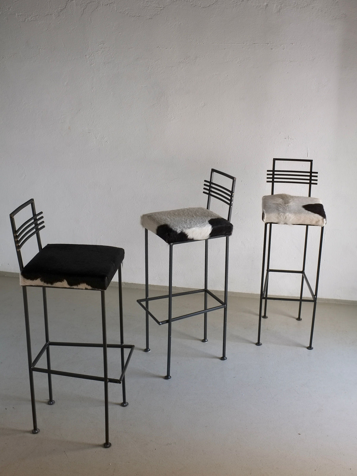 Three wrought iron bar stools with cowhide seats in minimalist setting