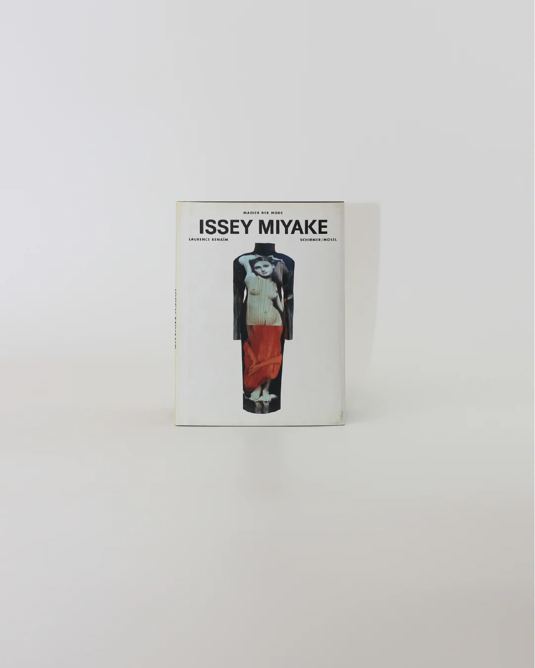 The cover of the "Issey Miyake Book" from Boga Avante Shop features a model dressed in a layered outfit that beautifully highlights the designer's iconic pleating techniques. The ensemble consists of a coat, top, and striking red pants against a simple white backdrop, effortlessly capturing the essence of contemporary fashion.