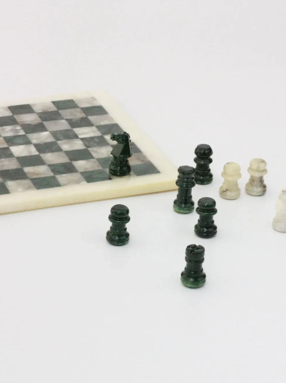 A *Vintage Green and White Marble Chessboard* by *Boga Avante Shop* is set on a white surface. Some pieces stand on the board while several others are scattered off the board. The handmade marble board has a mix of dark and light squares, and the pieces are in mid-game arrangement, creating an elegant set.