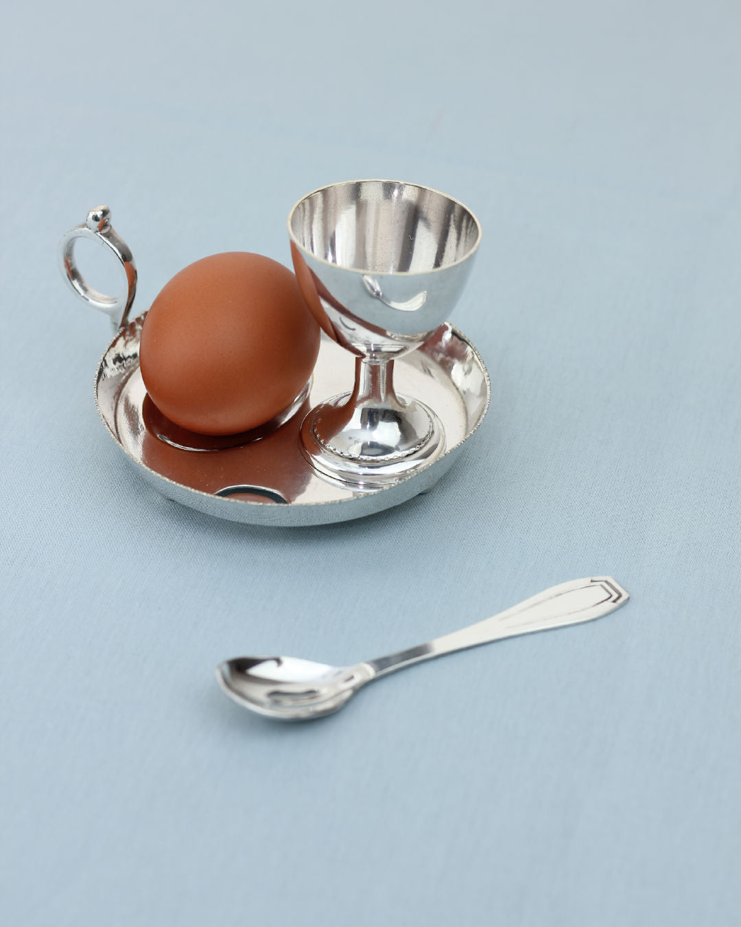 Silver egg cup with handle on tray, brown egg and spoon detail