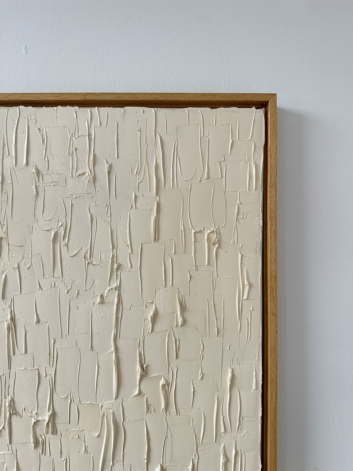 A close-up of "Warm White," an oil on canvas by Roi Elmaliah, showcases off-white, thick rectangular brush strokes that beautifully capture the essence of Amsterdam's artistic vibe. The piece is elegantly framed with a simple wooden border, providing a striking contrast between the smooth wood and the rough texture of the artwork.