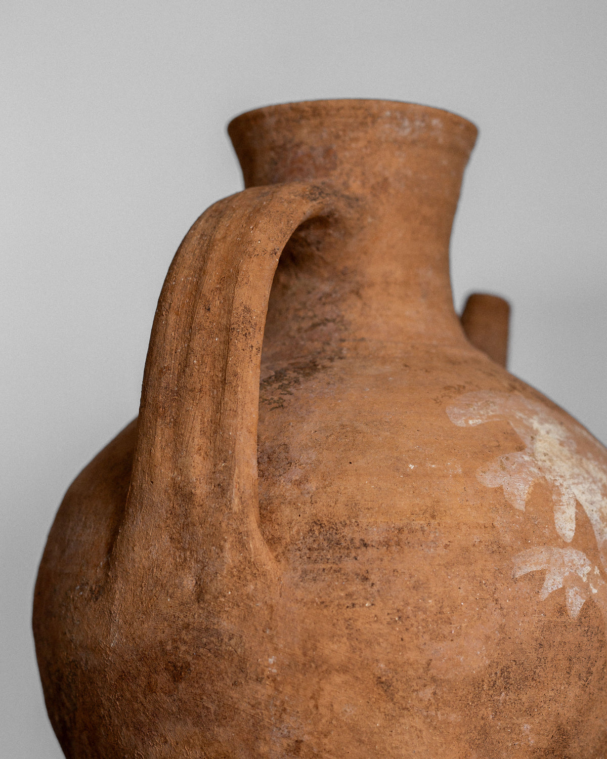 A close-up of the Early 20th Century European Ceramic Pitcher by Spigel, a hand-crafted terracotta jug featuring a wide, rounded body, narrow neck, single curved handle, and faint white floral patterns that enrich its rustic charm.