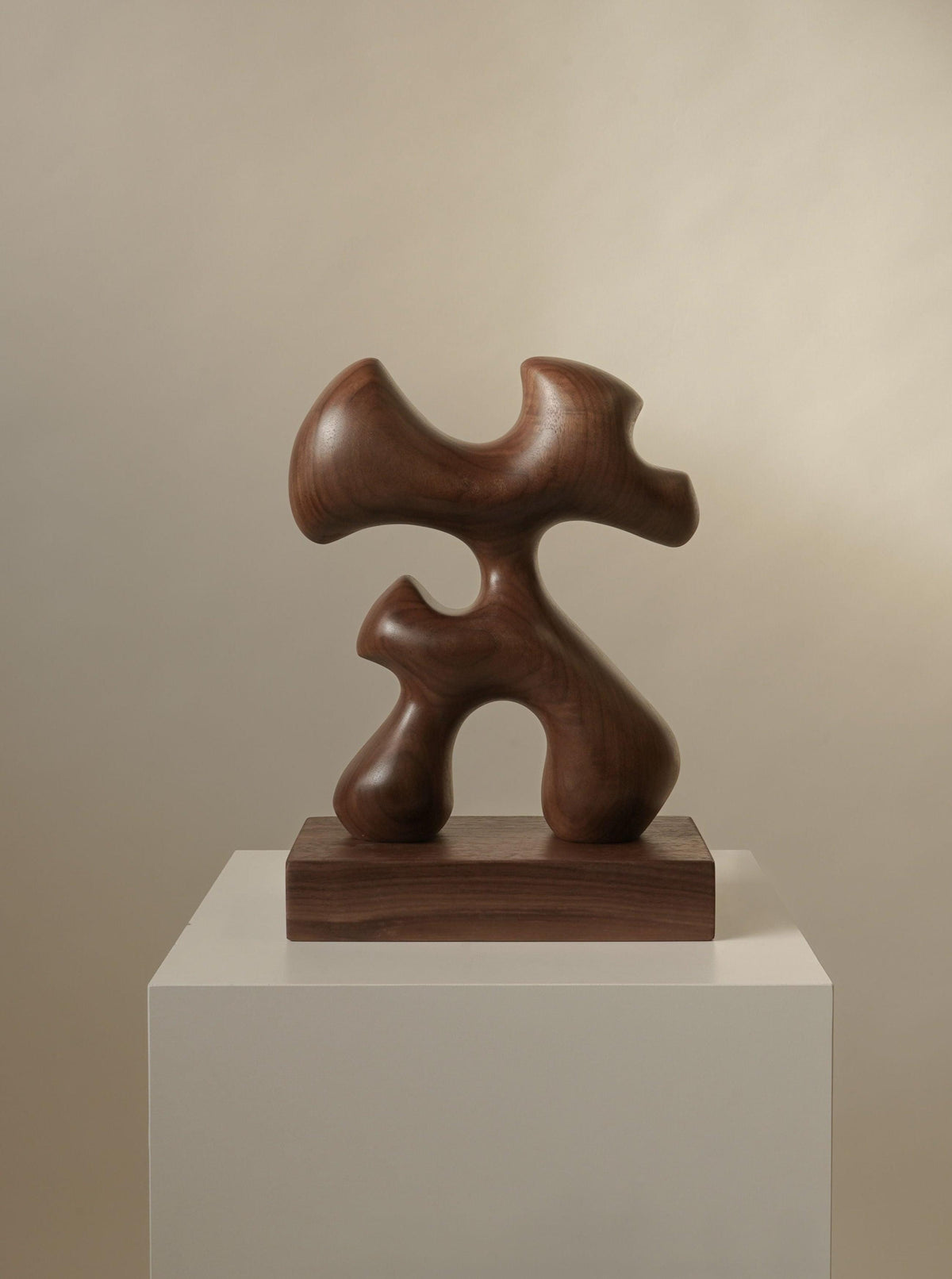 The handcrafted Abari sculpture by Chandler McLellan features smooth curves and intersecting shapes on a rectangular base. Set against a neutral background, it embodies contemporary design and serves as collectible furniture.