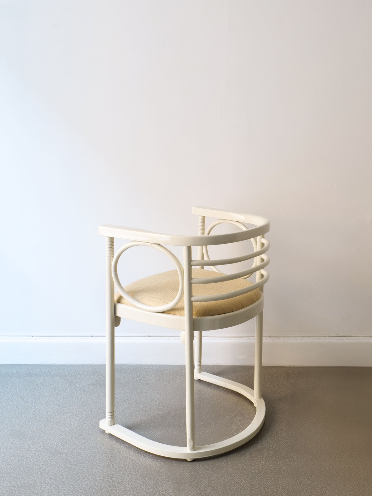 A Thonet Bentwood Chair by Josef Hoffman, part of the Collection apart brand, in a modern white finish, is placed in front of a light gray wall and floor. Its minimalist design showcases circular armrests and a round wooden seat, embodying the elegance of lacquered bentwood armchairs.