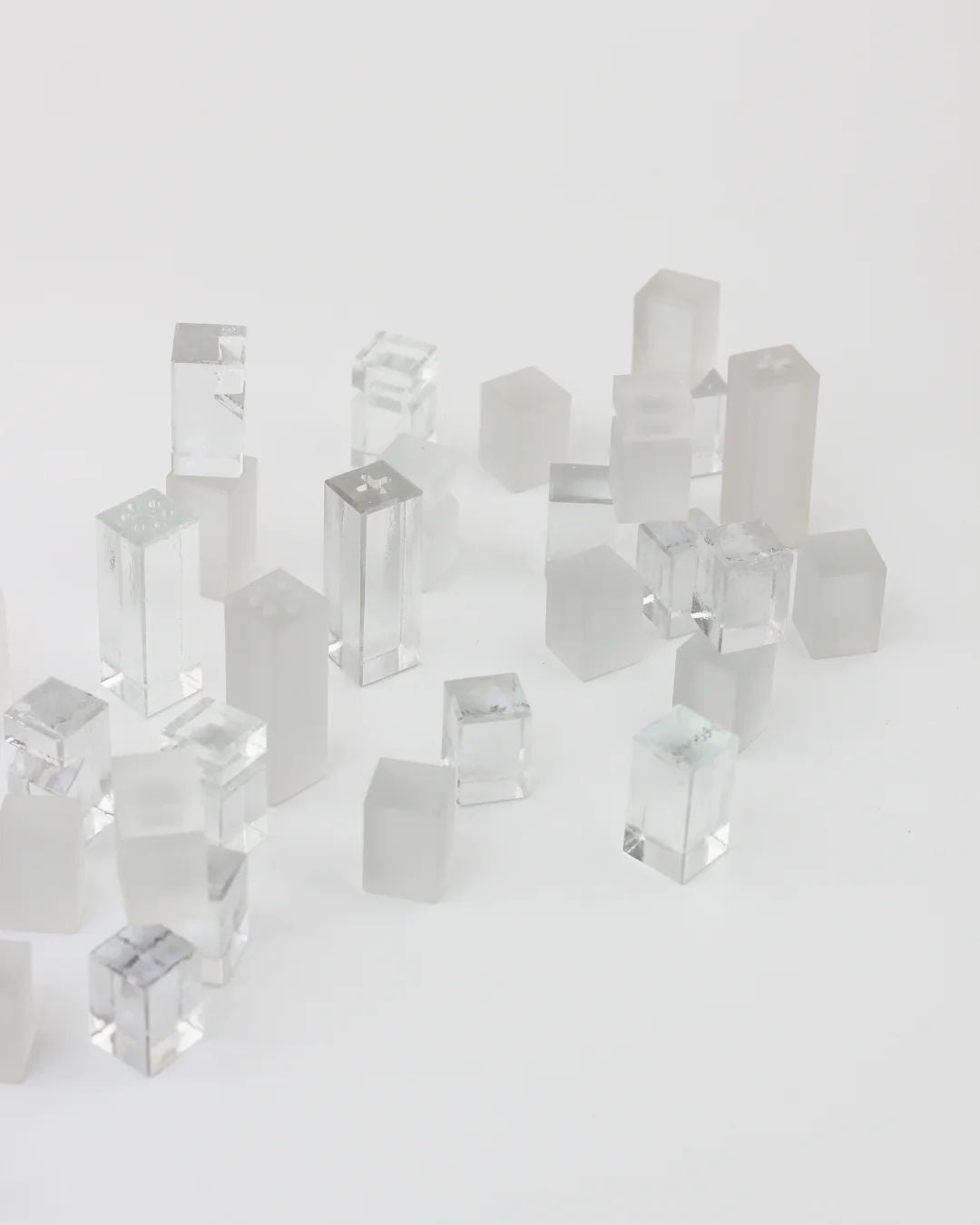 Clear and frosted acrylic cubes and rectangular prisms from the Crystal Chess Set by Boga Avante Shop are arranged on a white surface, creating a minimalist, abstract design inspired by a crystal chess set.