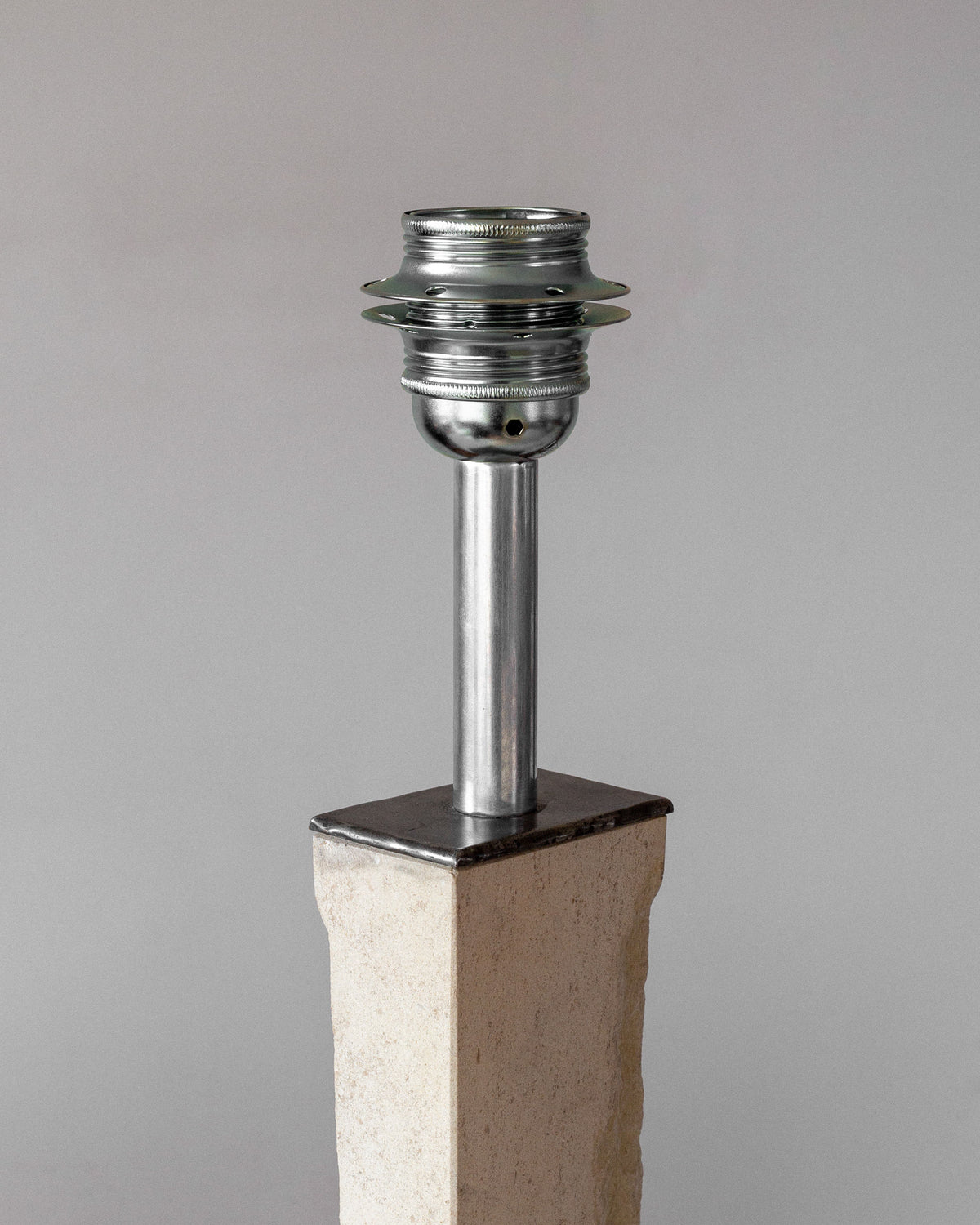 A Spigel Modernist Travertine and Metal Table Lamp features an Art Deco-inspired design with a metal cylindrical fixture on a rectangular stone base, resembling an industrial light socket against a neutral background.