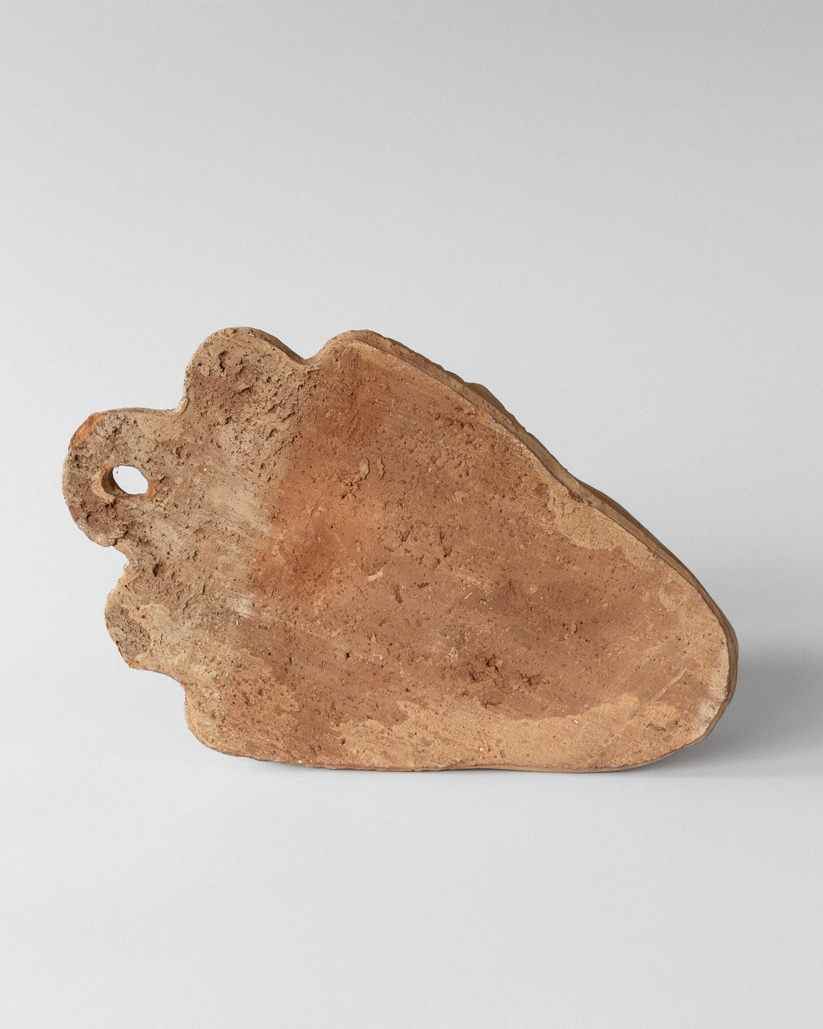 The Spigel Terracotta Wall Mask Planter, with an uneven surface and rich visible grain, resembles a rustic wooden cutting board against a plain white background, echoing the timeless charm of unglazed terra cotta pottery.